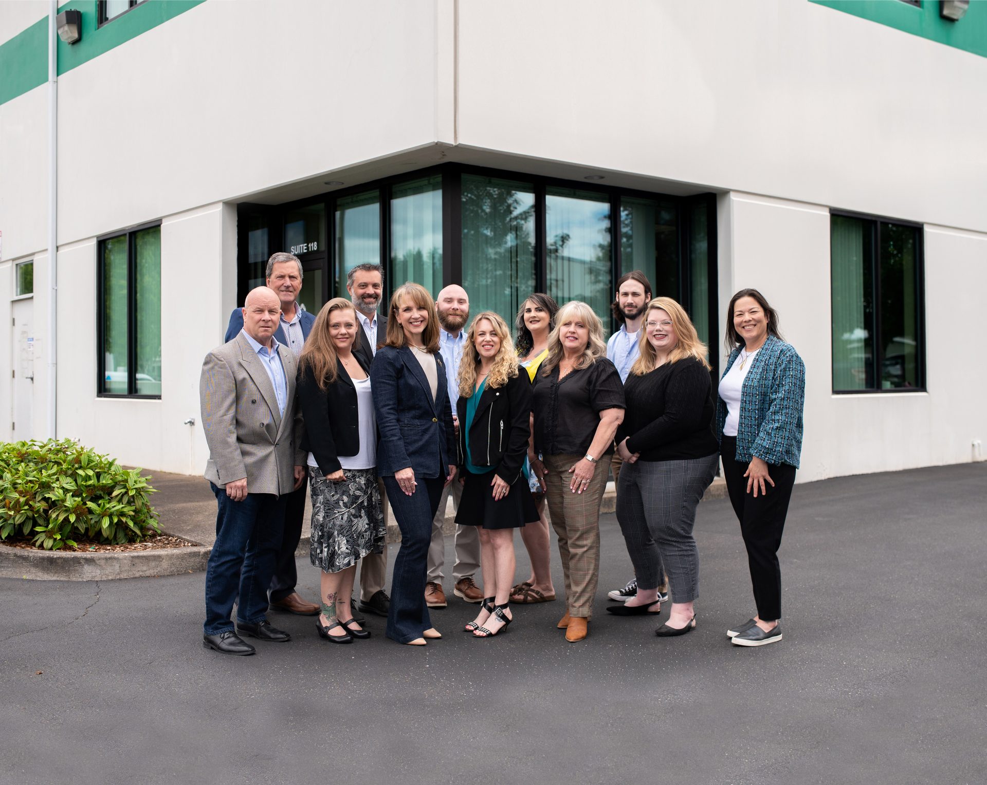 A diverse group of men and women from a company team stands outside a modern office building.