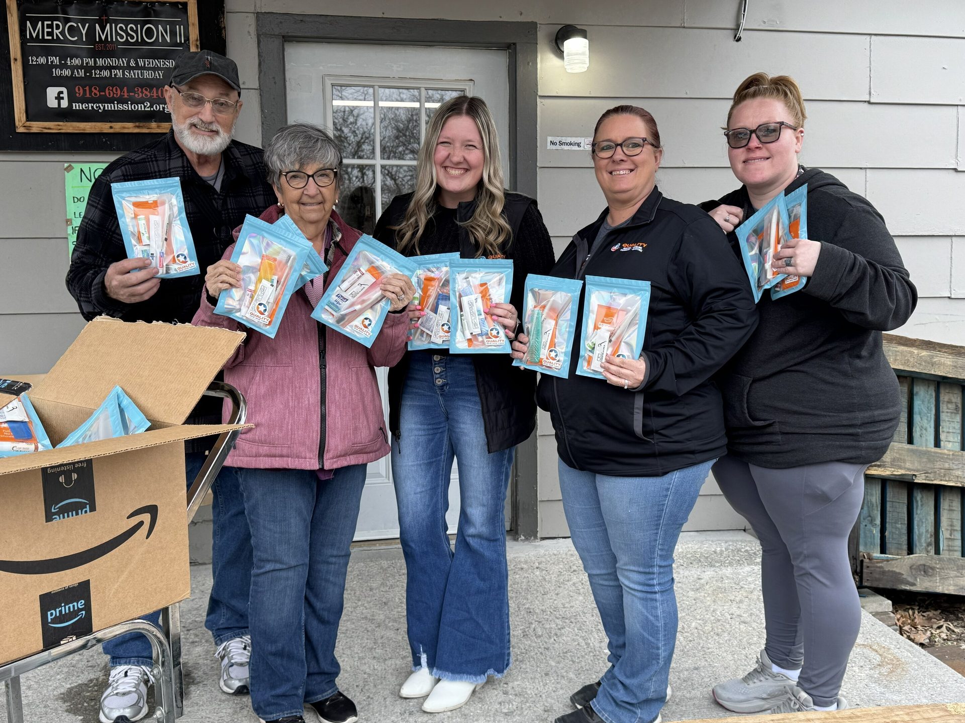 Five people hold hygiene kits outside Mercy Mission II, distributing aid to the community.