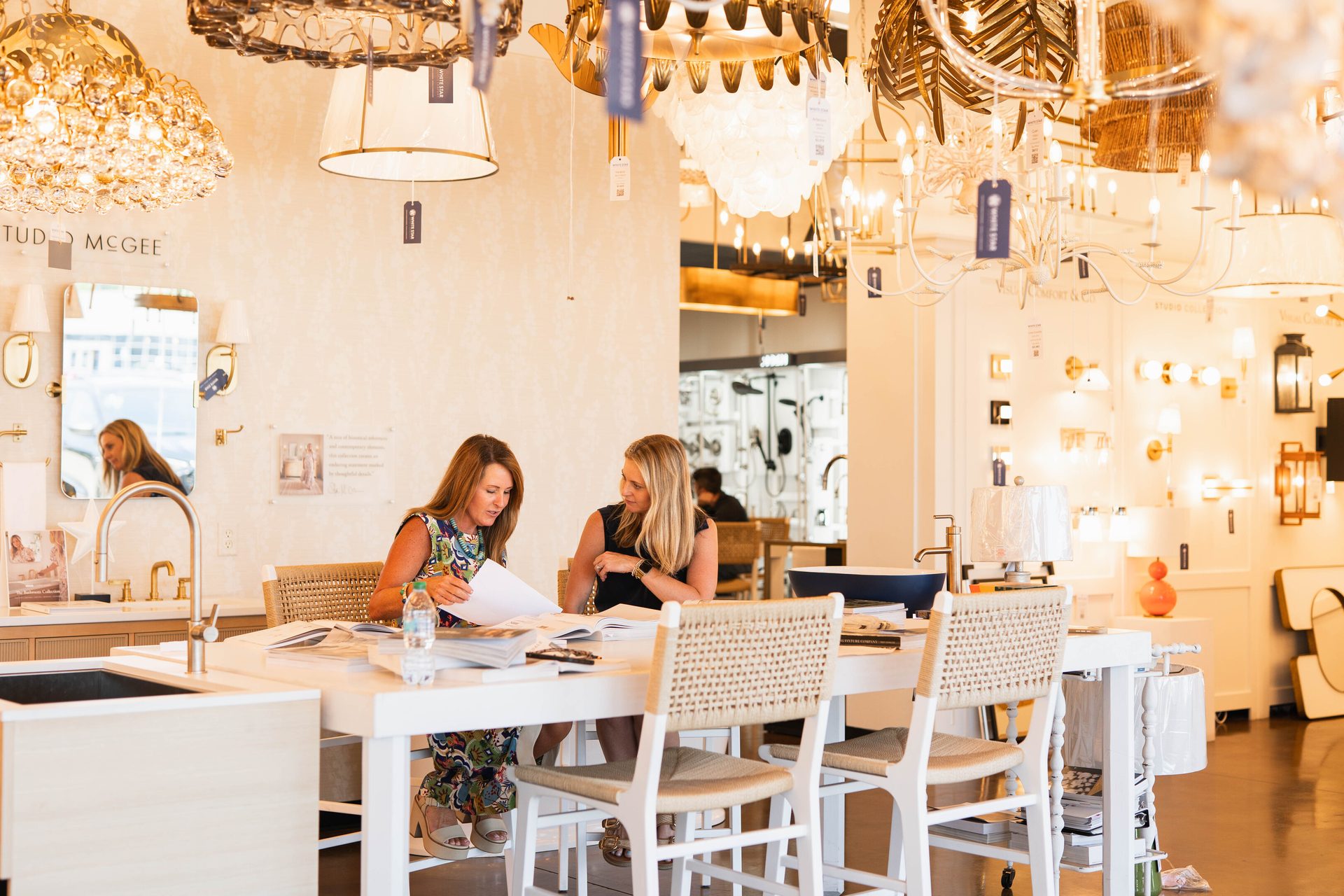 Two women review papers at a table in a stylish lighting showroom.