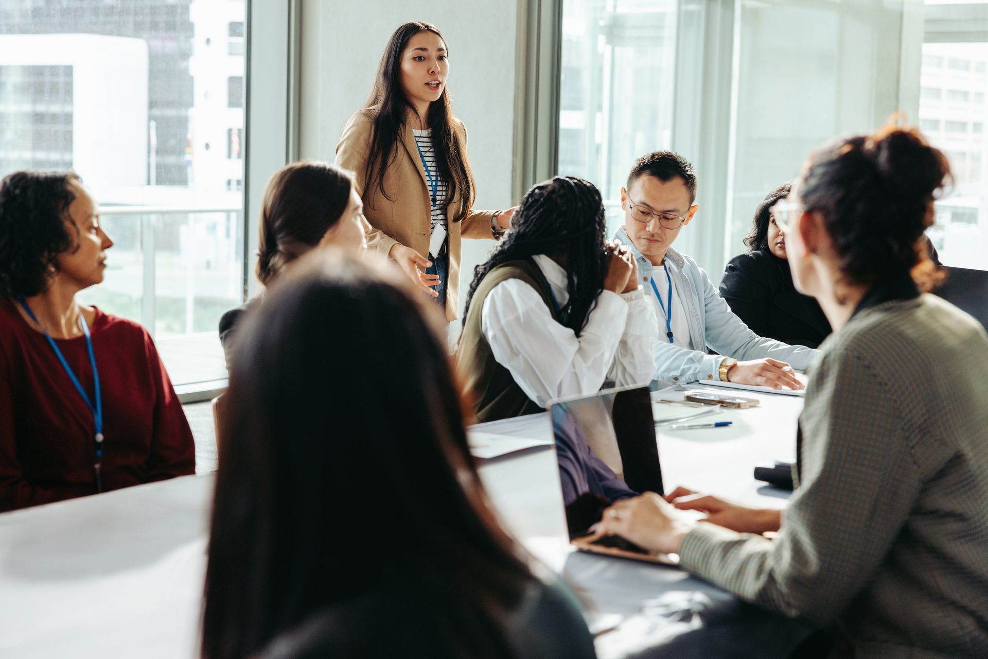 A diverse group of professionals in a bright meeting room, with one woman standing and speaking.