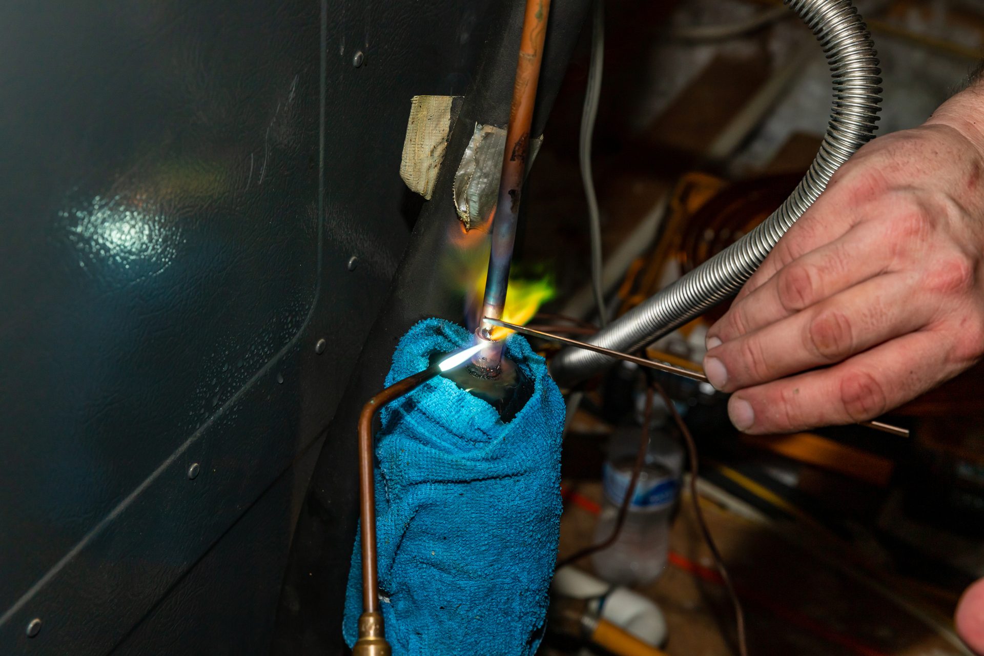 Hand brazing copper pipe with a torch, bright flame, and a protective blue rag.