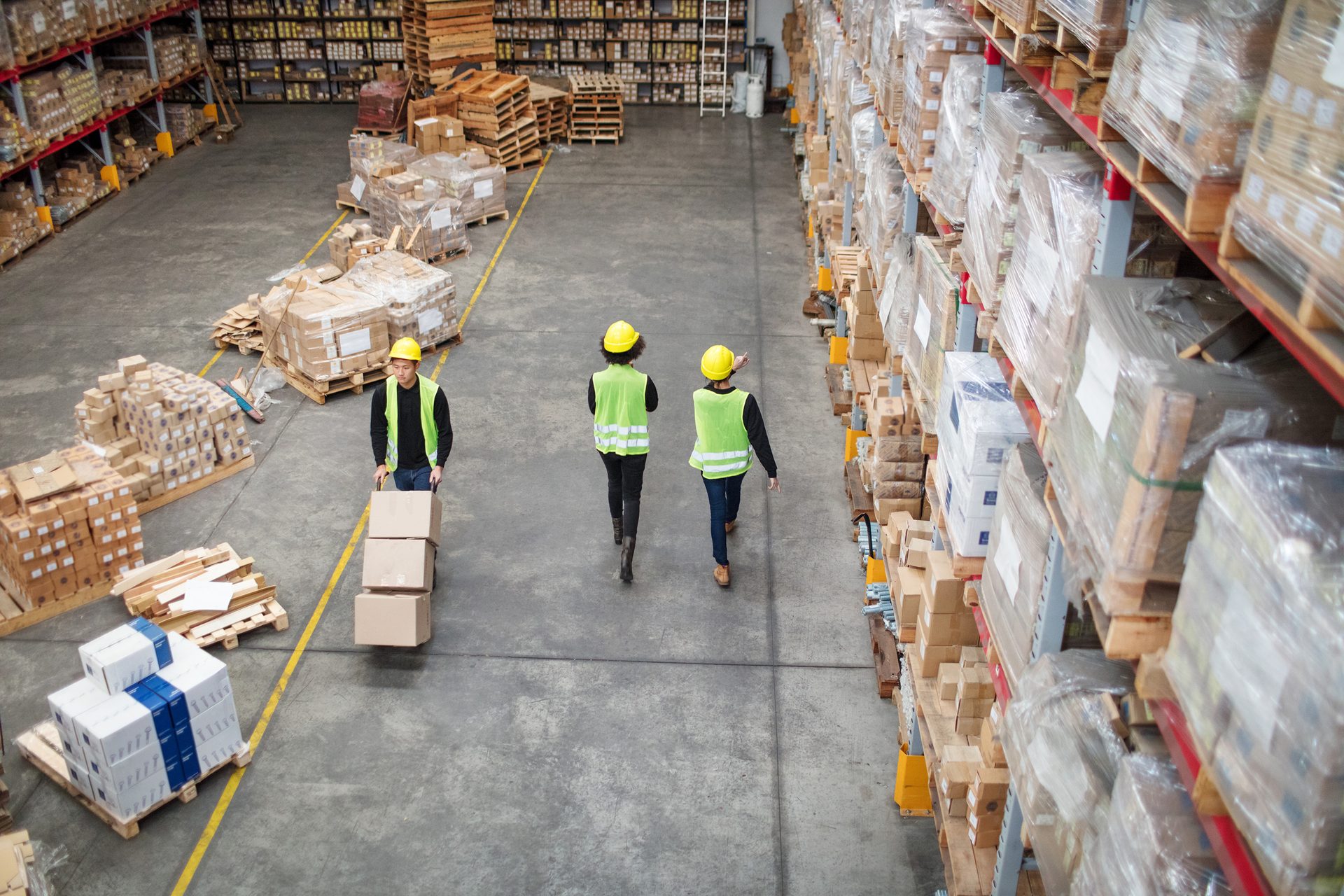 Overhead view of three workers and shelves packed with boxes in a large warehouse.