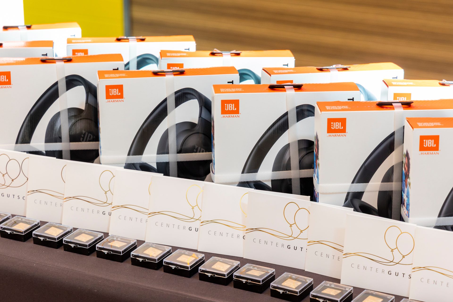 JBL headphone boxes, 'CENTERGUTS' cards with gold balloon graphics, and small golden items on a table.