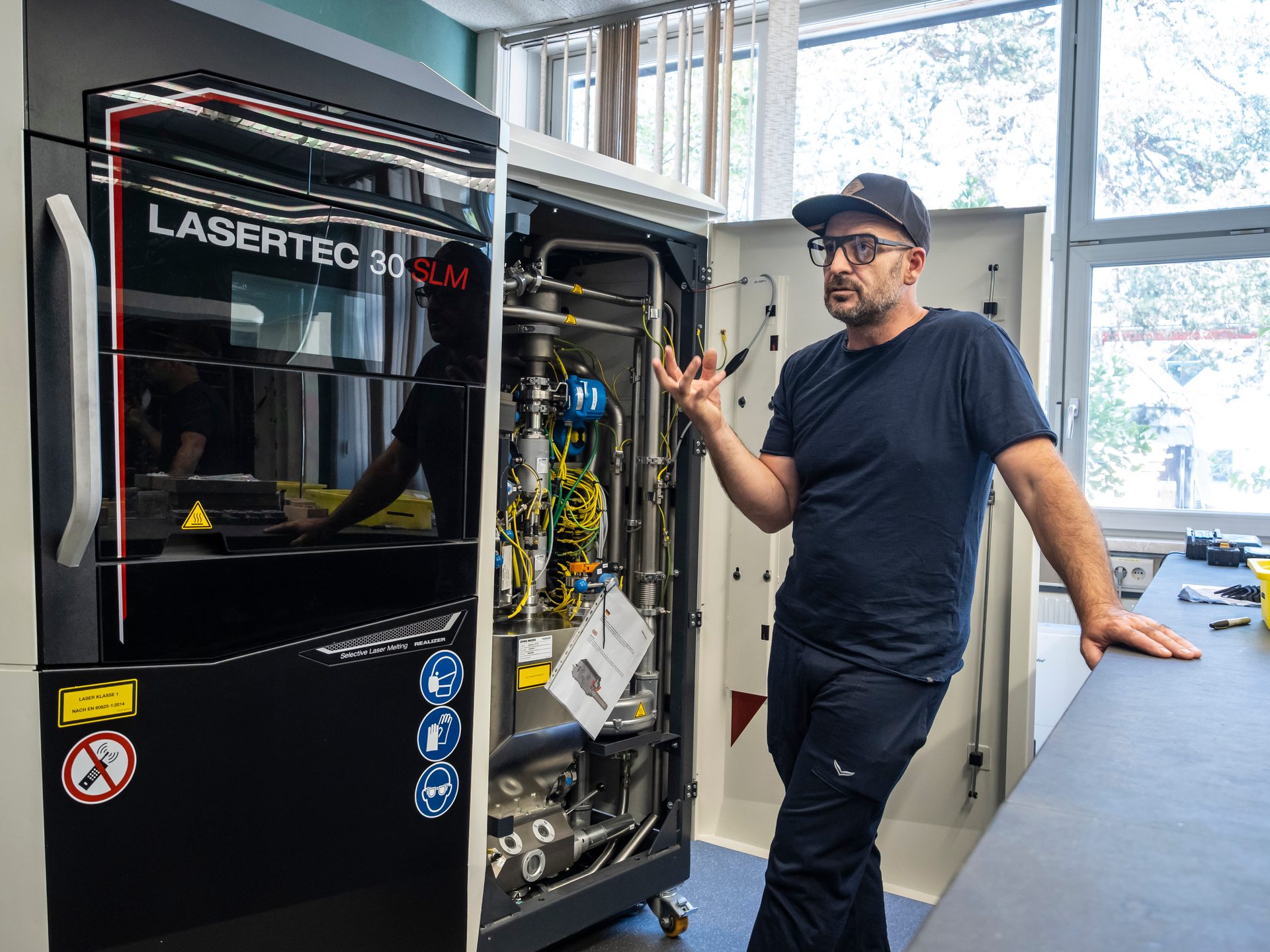 A man explains an open LASERTEC 30 SLM machine, revealing its internal components.