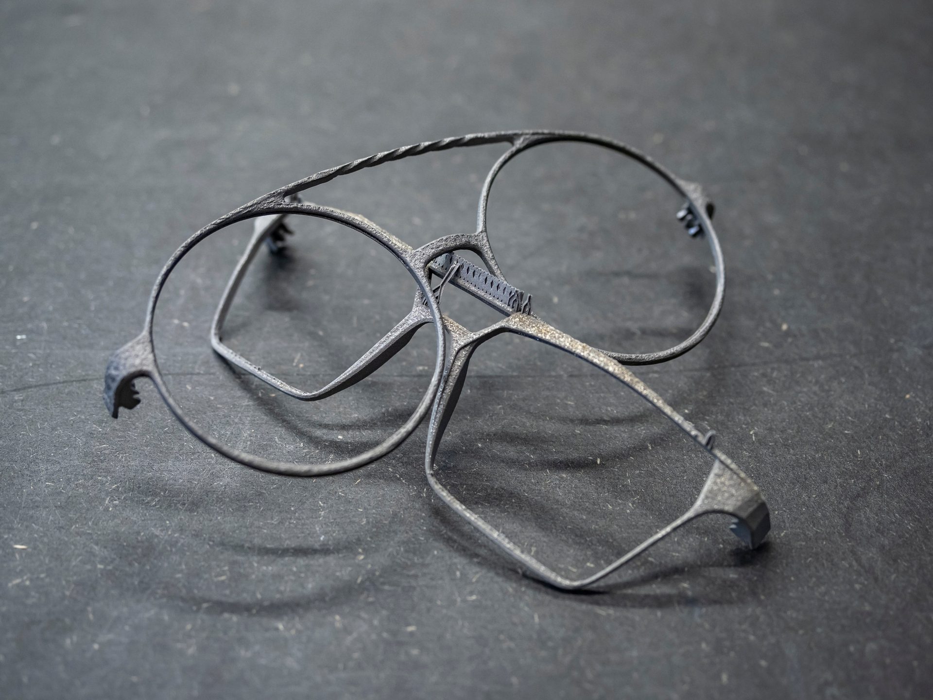 Broken, dark 3D-printed glasses frames on a dark surface.