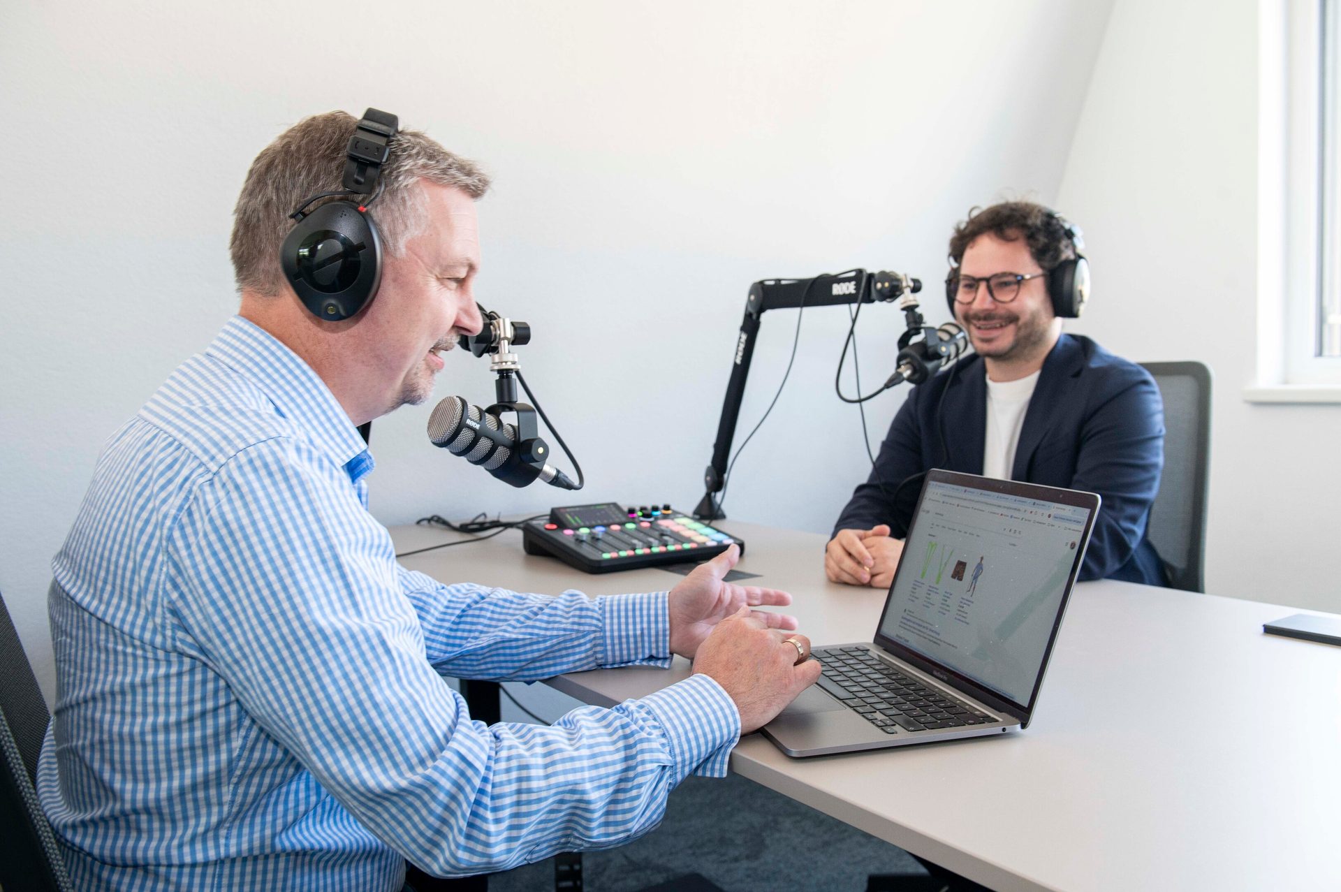 Two men podcasting with microphones, headphones, and a laptop.