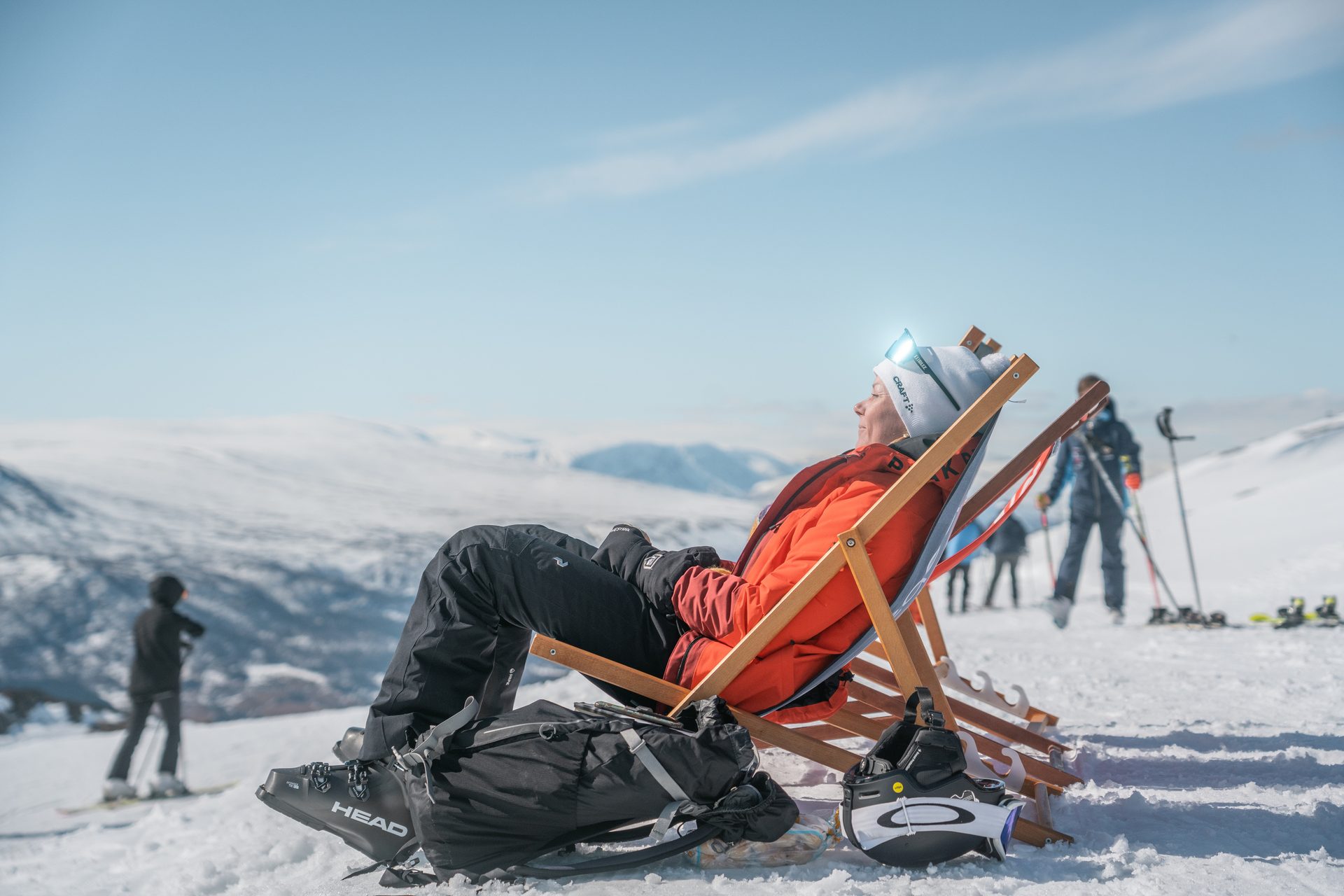Person relaxing in a deck chair on a snowy mountain, enjoying the sun. Ski gear nearby.