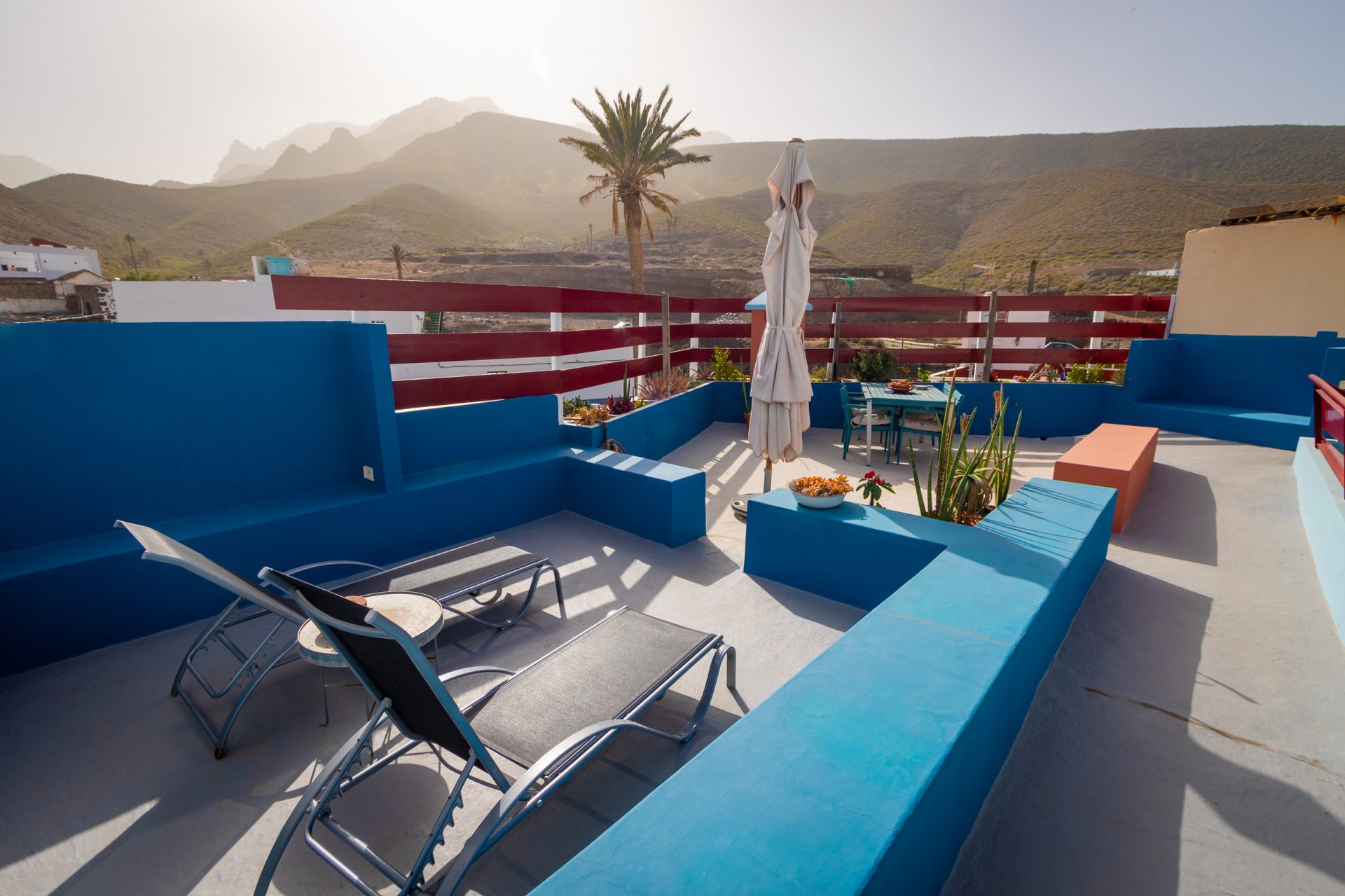 Blue rooftop terrace with seating, dining, and scenic hazy mountain views.