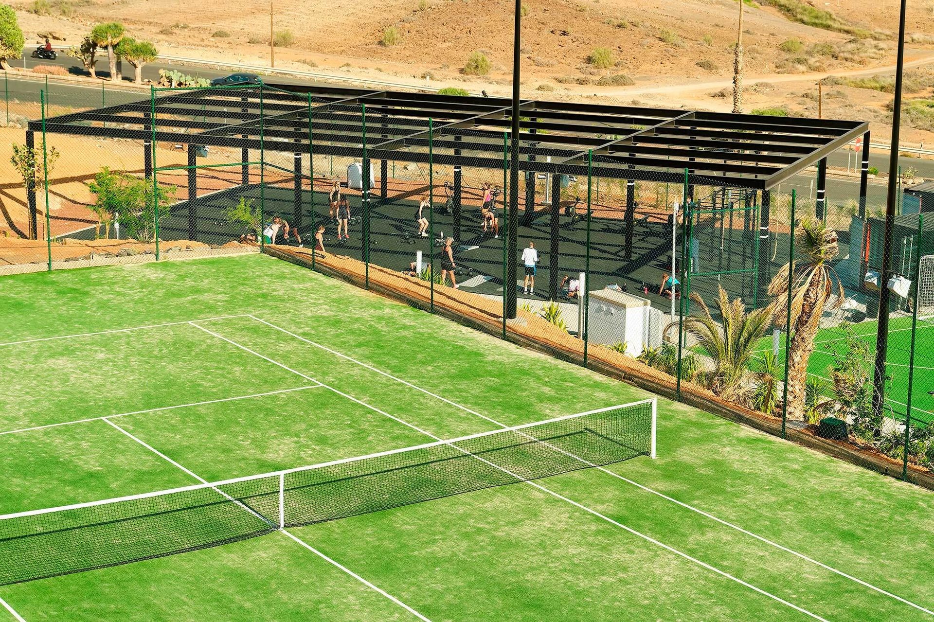 A tennis court in the foreground, with an outdoor gym and people exercising in the background.