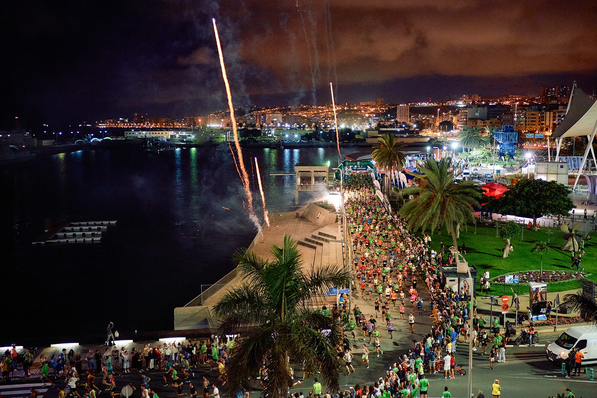 Night marathon with fireworks, runners, and a city skyline next to a harbor.