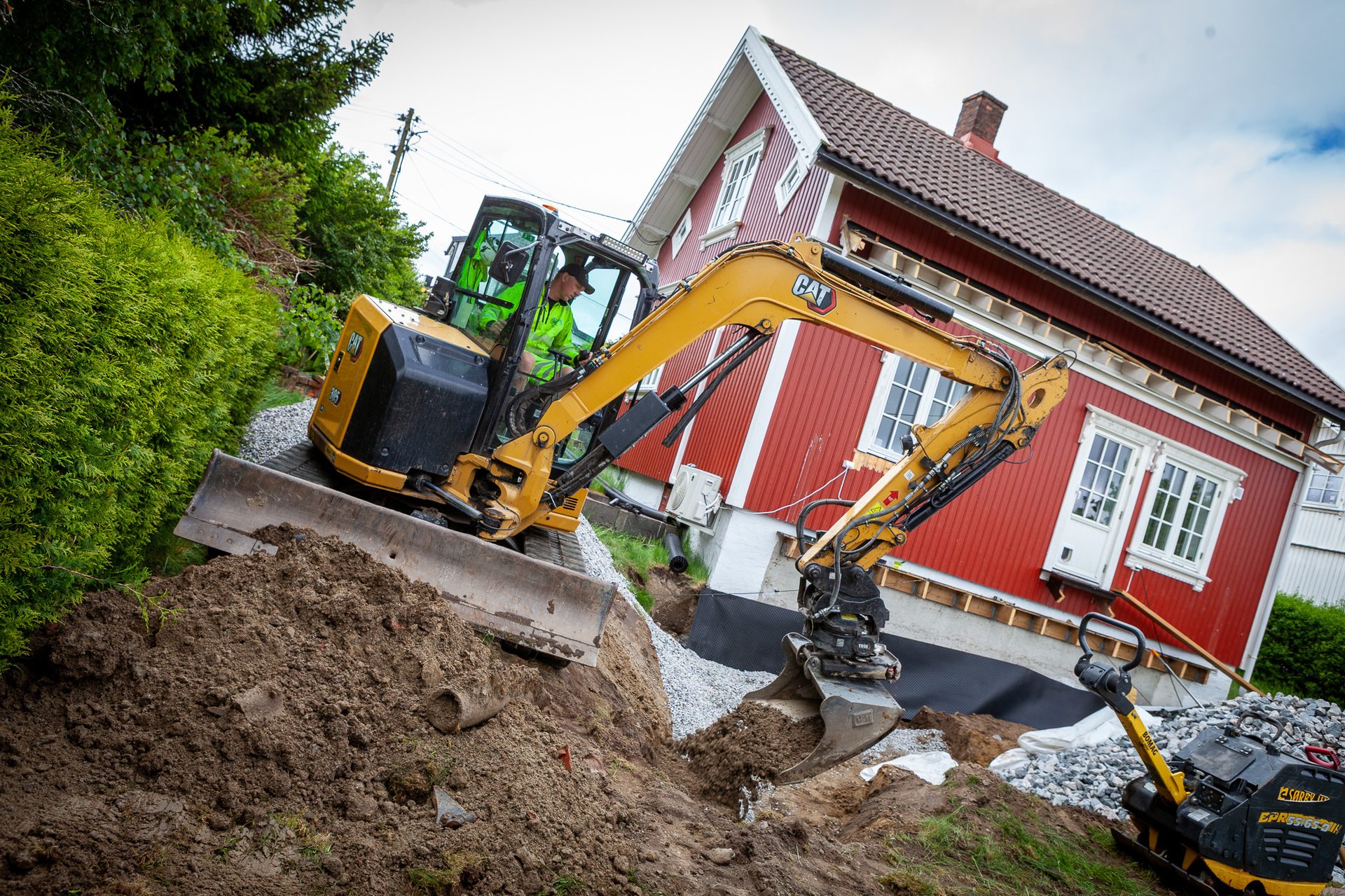 Yellow excavator digging dirt next to a red house.
