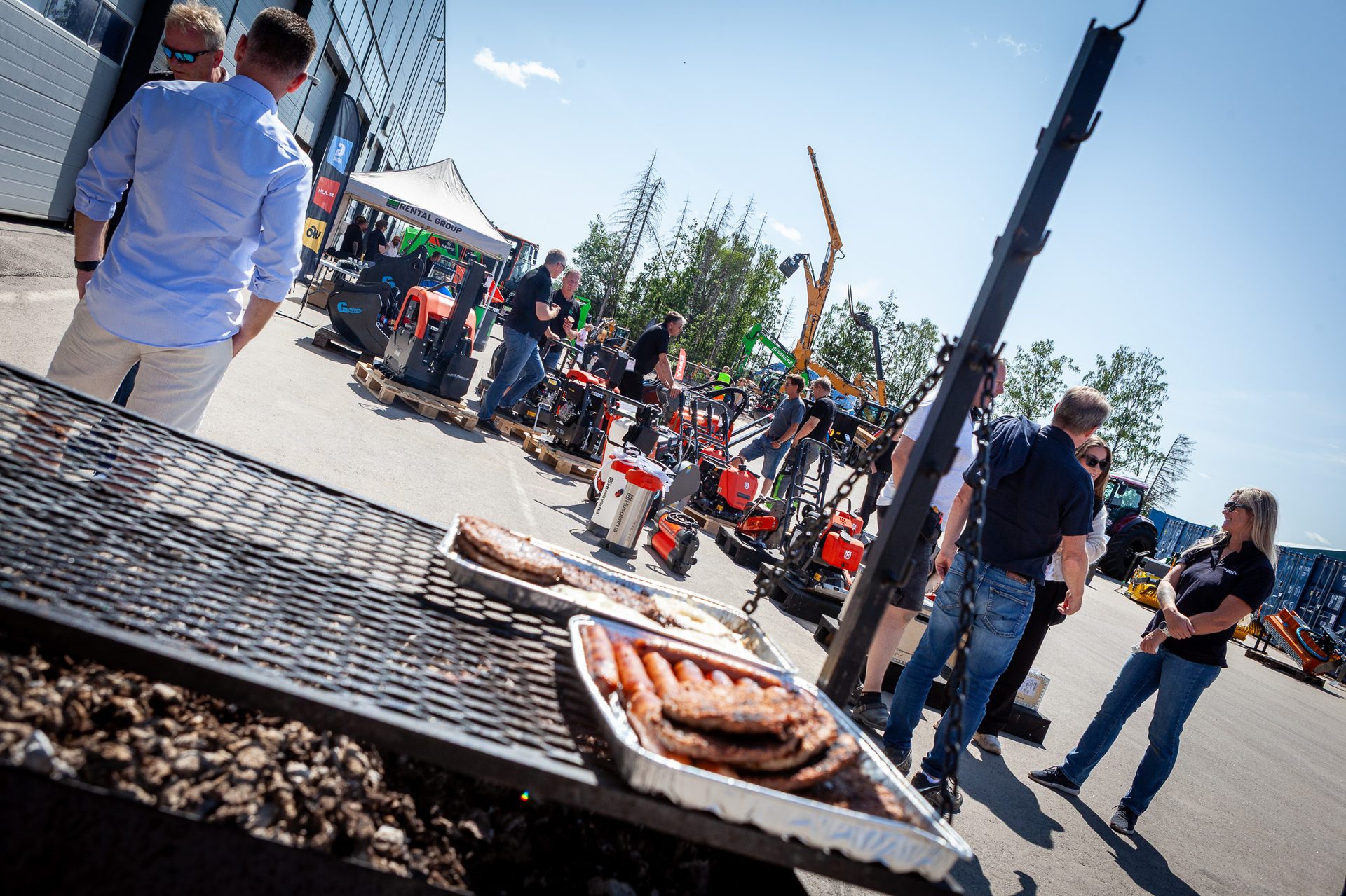 Outdoor machinery display with people, and a BBQ grill with food in the foreground.