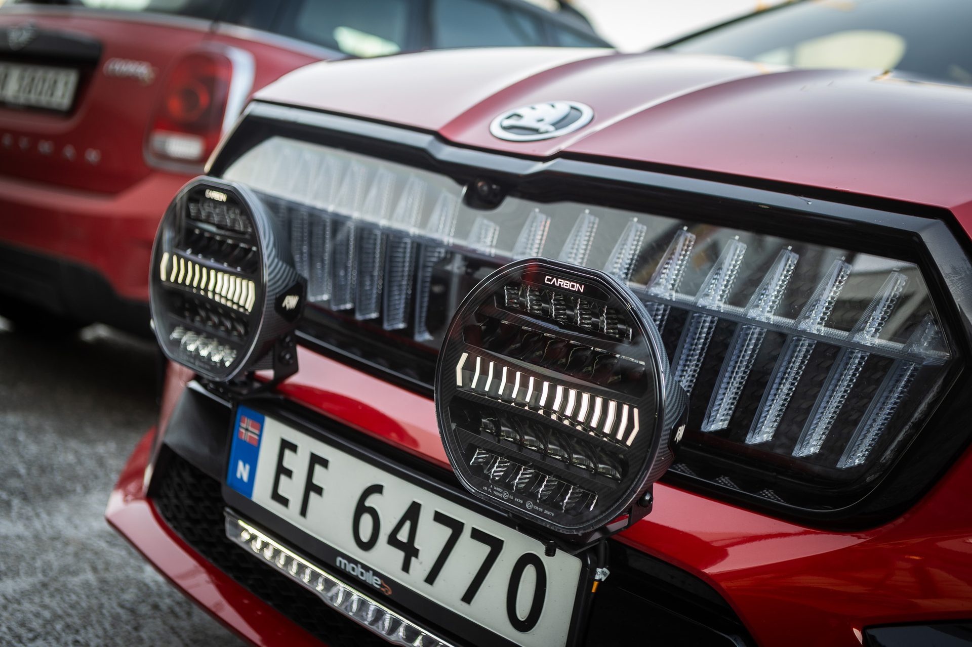 Front of a red car with round LED auxiliary lights and a Norwegian license plate.