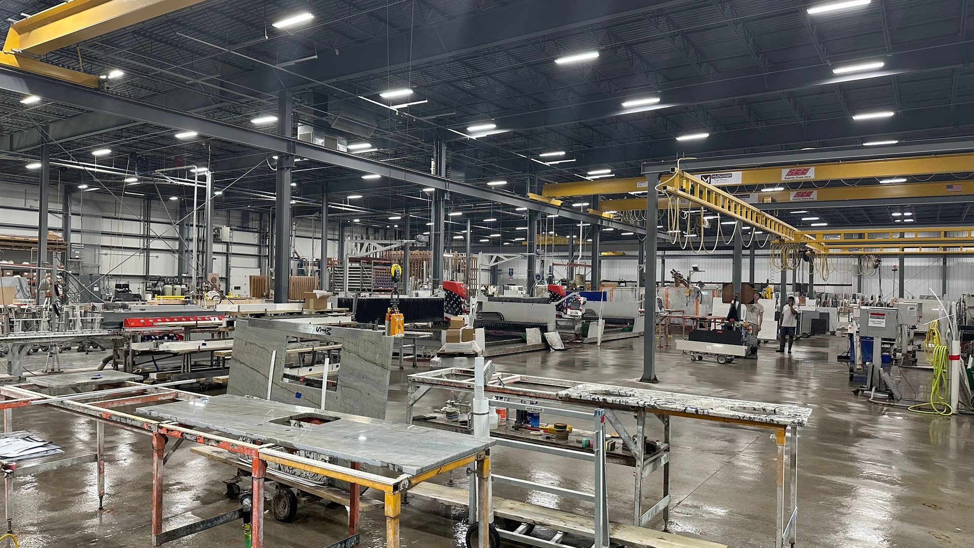Industrial stone workshop with machinery, countertops, and overhead cranes.