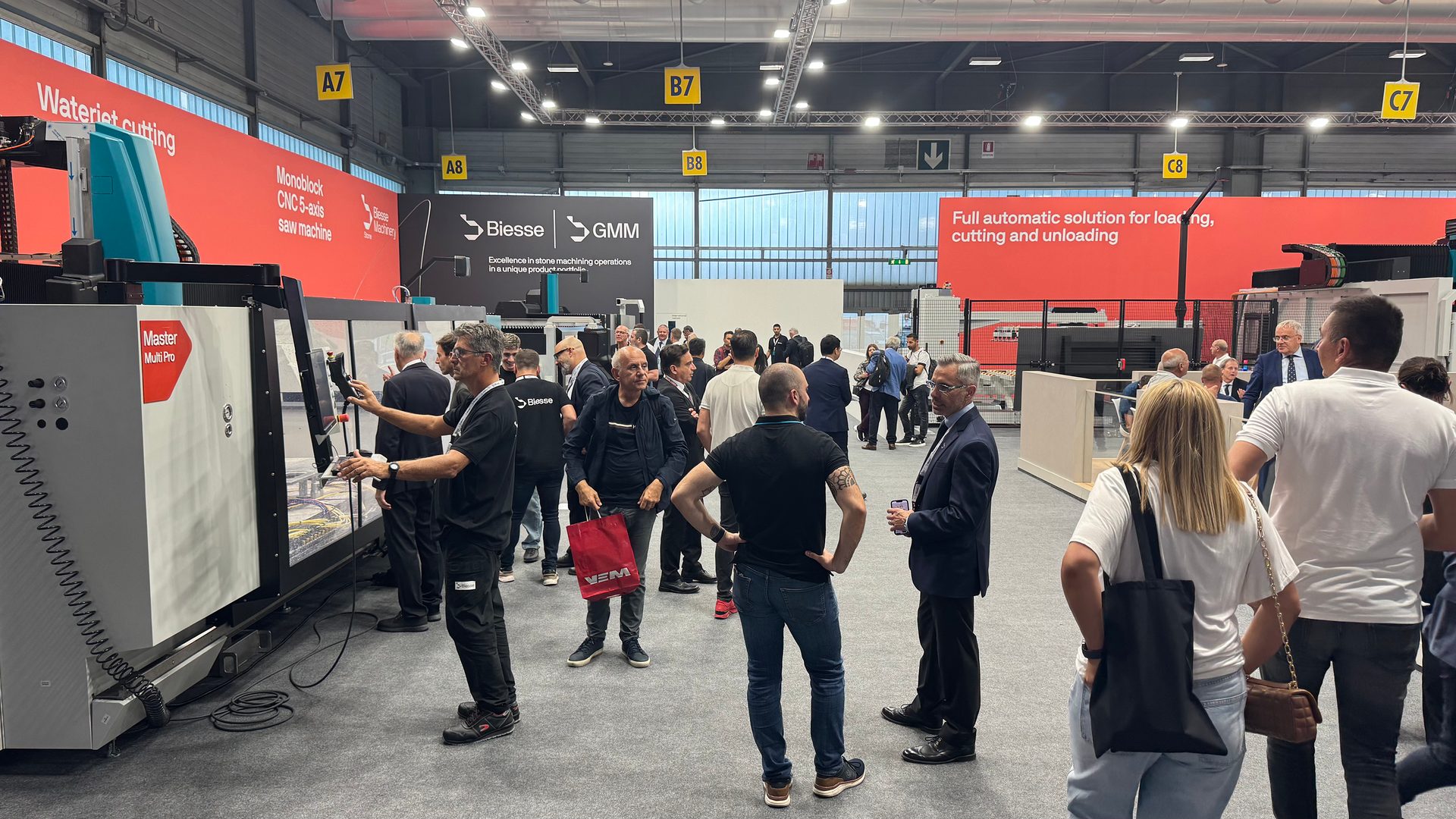 Trade show with attendees examining Biesse and GMM industrial cutting and machining equipment.
