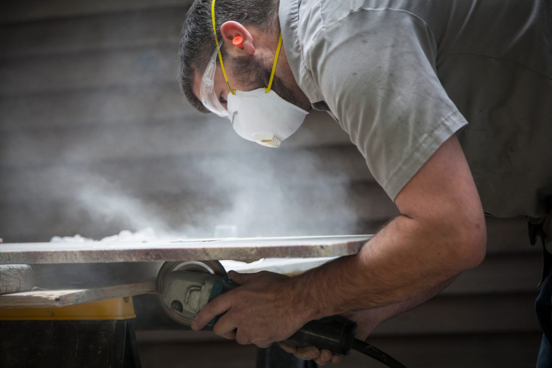 Man grinding granite or marble wearing a mask creating dust