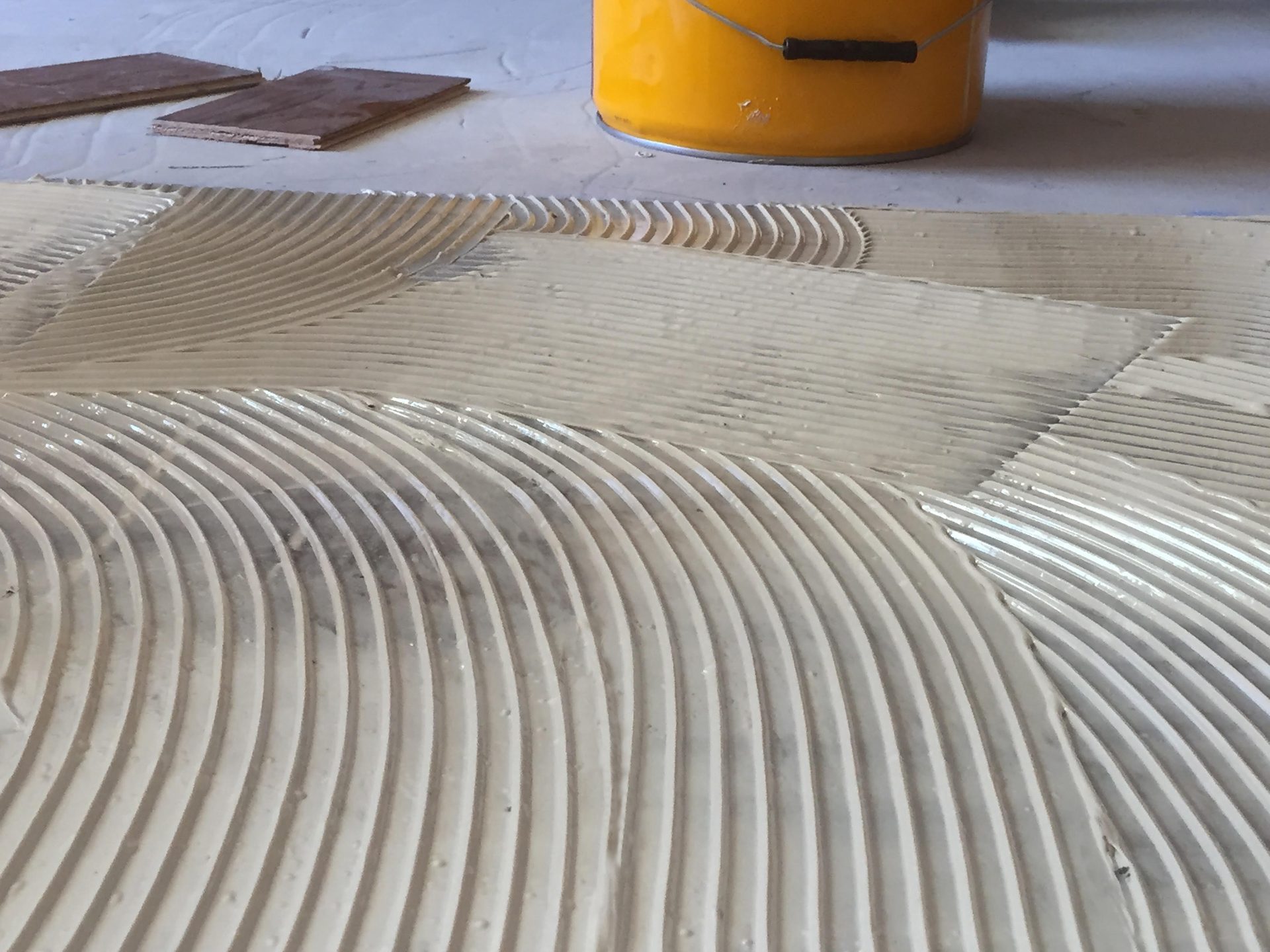 Floor adhesive with trowel ridges, wood planks, and yellow bucket.