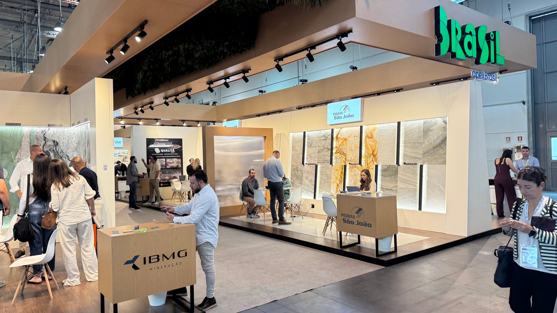Busy trade show booth for Brazilian stone companies, featuring Pedras São João and IBMG.
