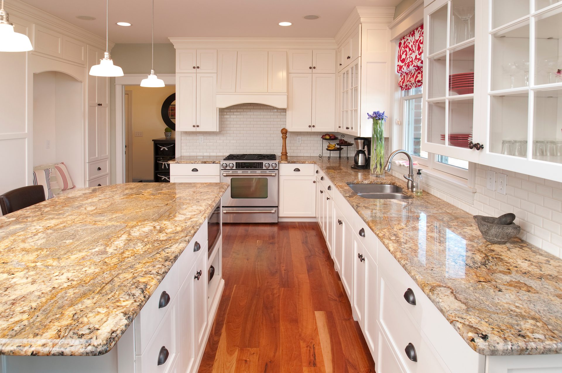 New modern kitchen with white cabinets, white subway tile backsplash and granite countertops showing warm brown veigolden tones throughout