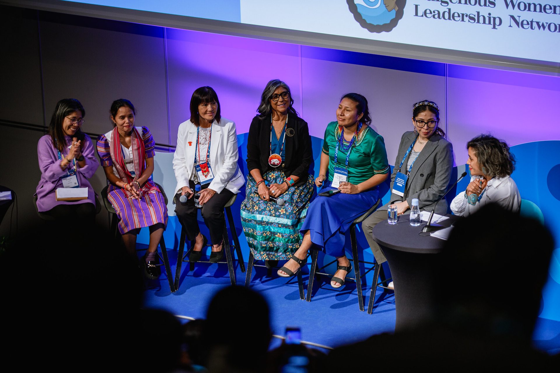 Seven women, some in traditional attire, smiling on a panel for the Indigenous Women Leadership Network.
