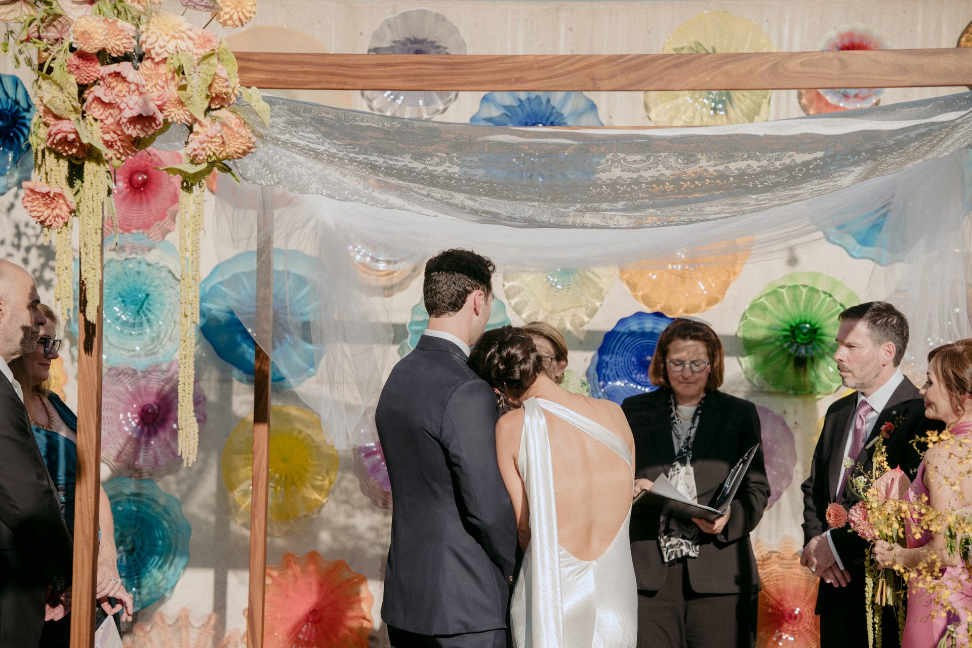Wedding ceremony with a couple, officiant, and a colorful glass art backdrop.