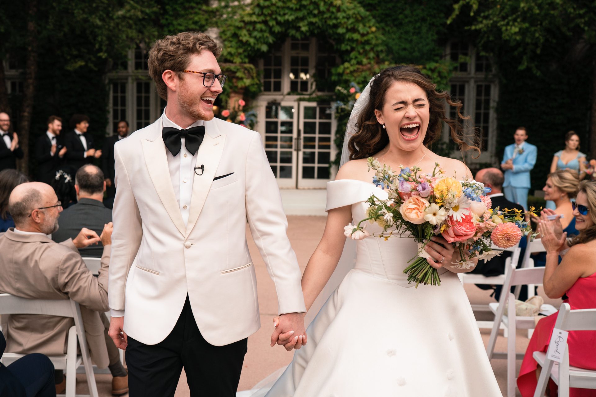 Elated bride and groom, hand-in-hand, laugh while walking down the aisle after their wedding.