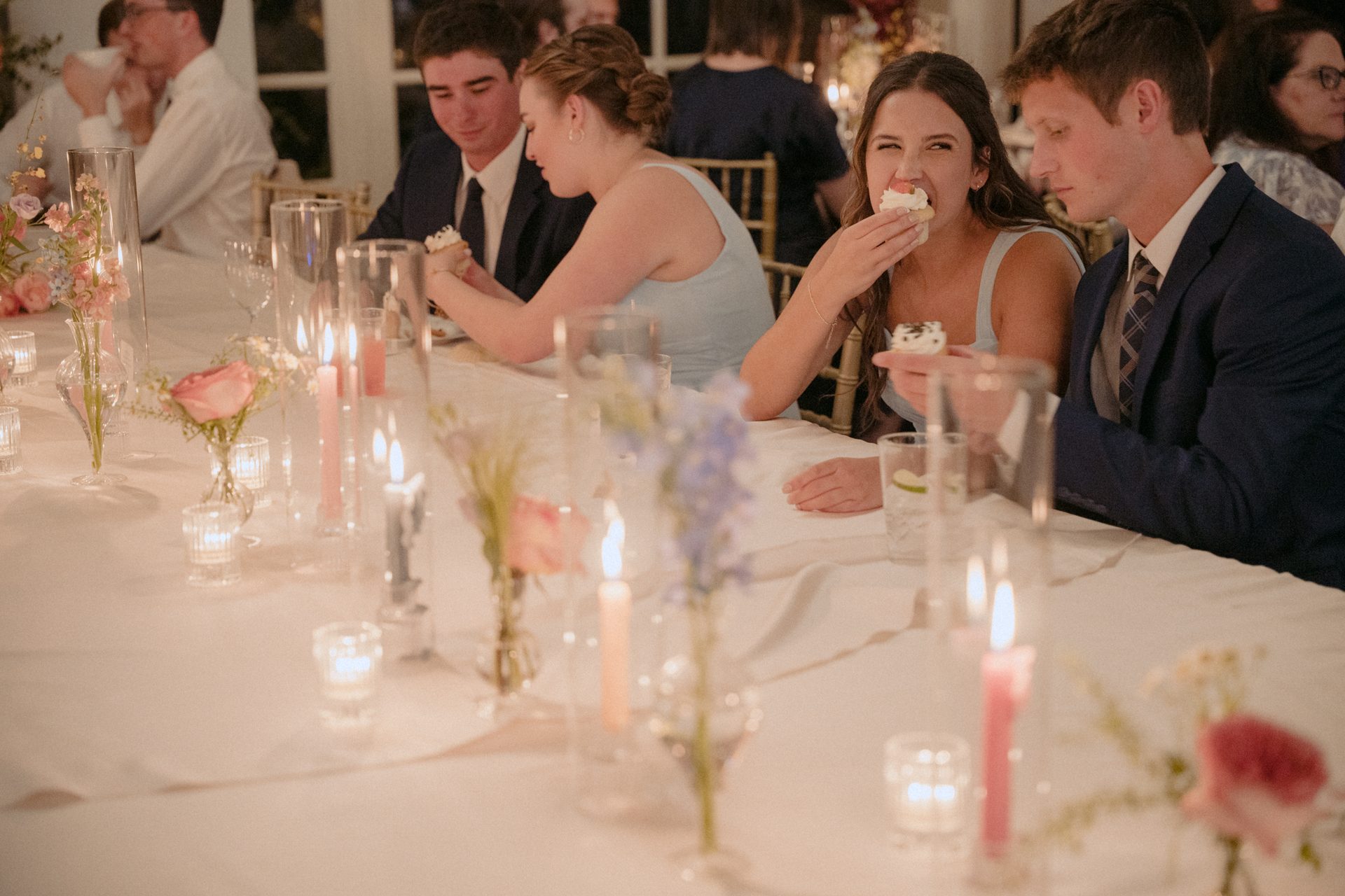 A woman eats a cupcake at a candlelit table with flowers and other guests.
