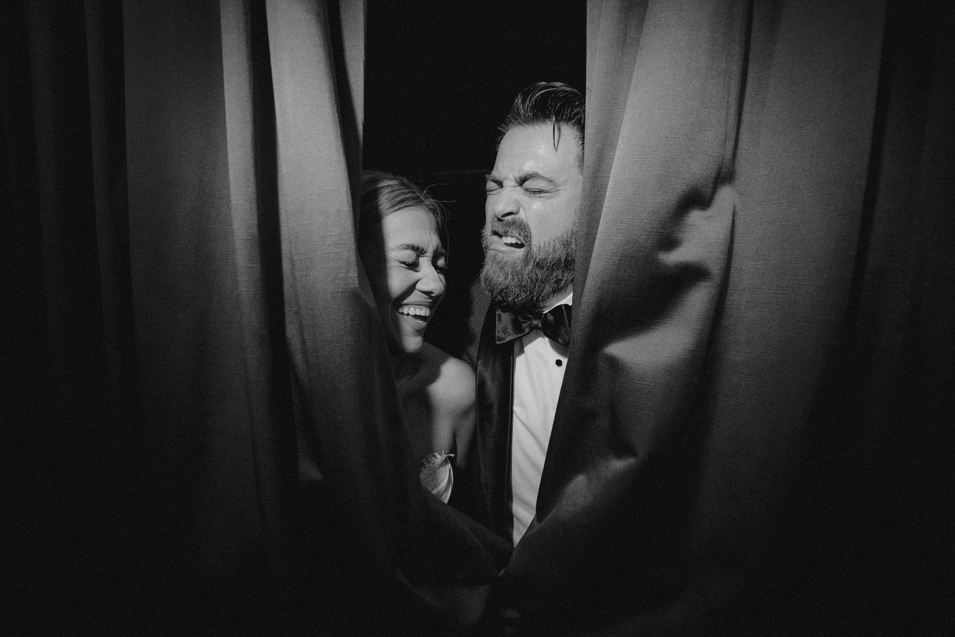 Laughing couple peeking through curtains, black and white.