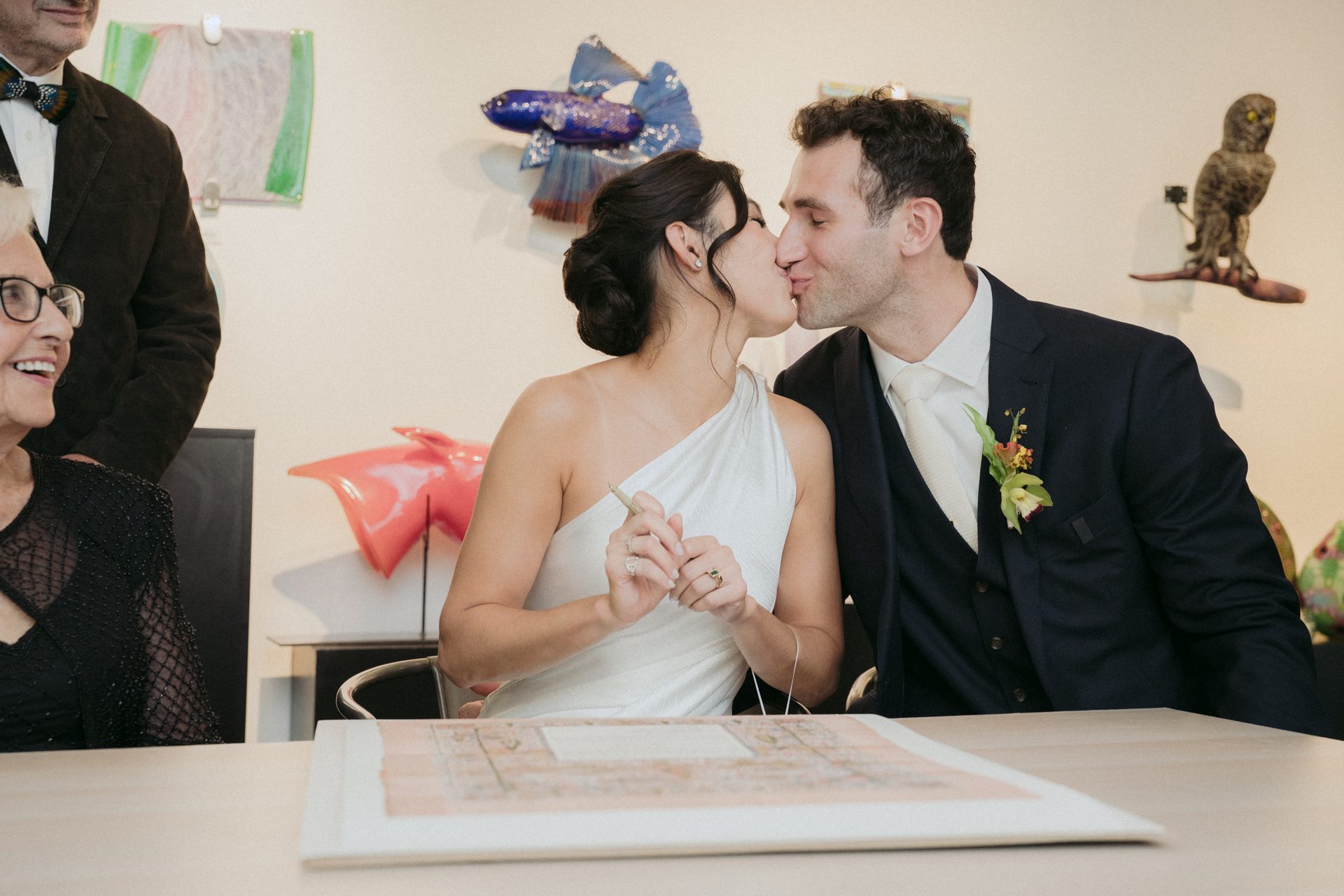Newlyweds kiss as the bride signs a marriage document.