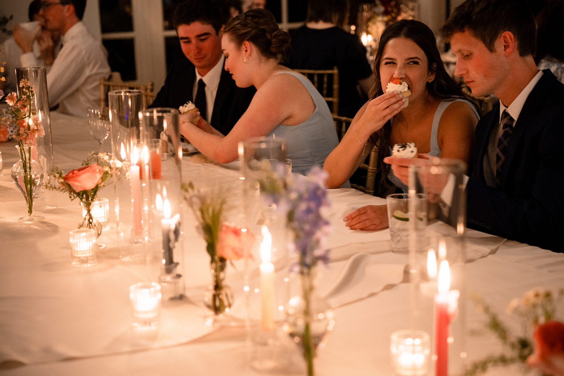 Guests at a candlelit table, one woman enjoying a cupcake.