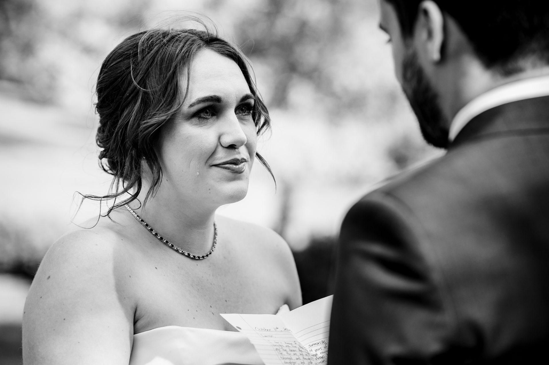 Tearful bride in black and white looks at groom while holding vows.