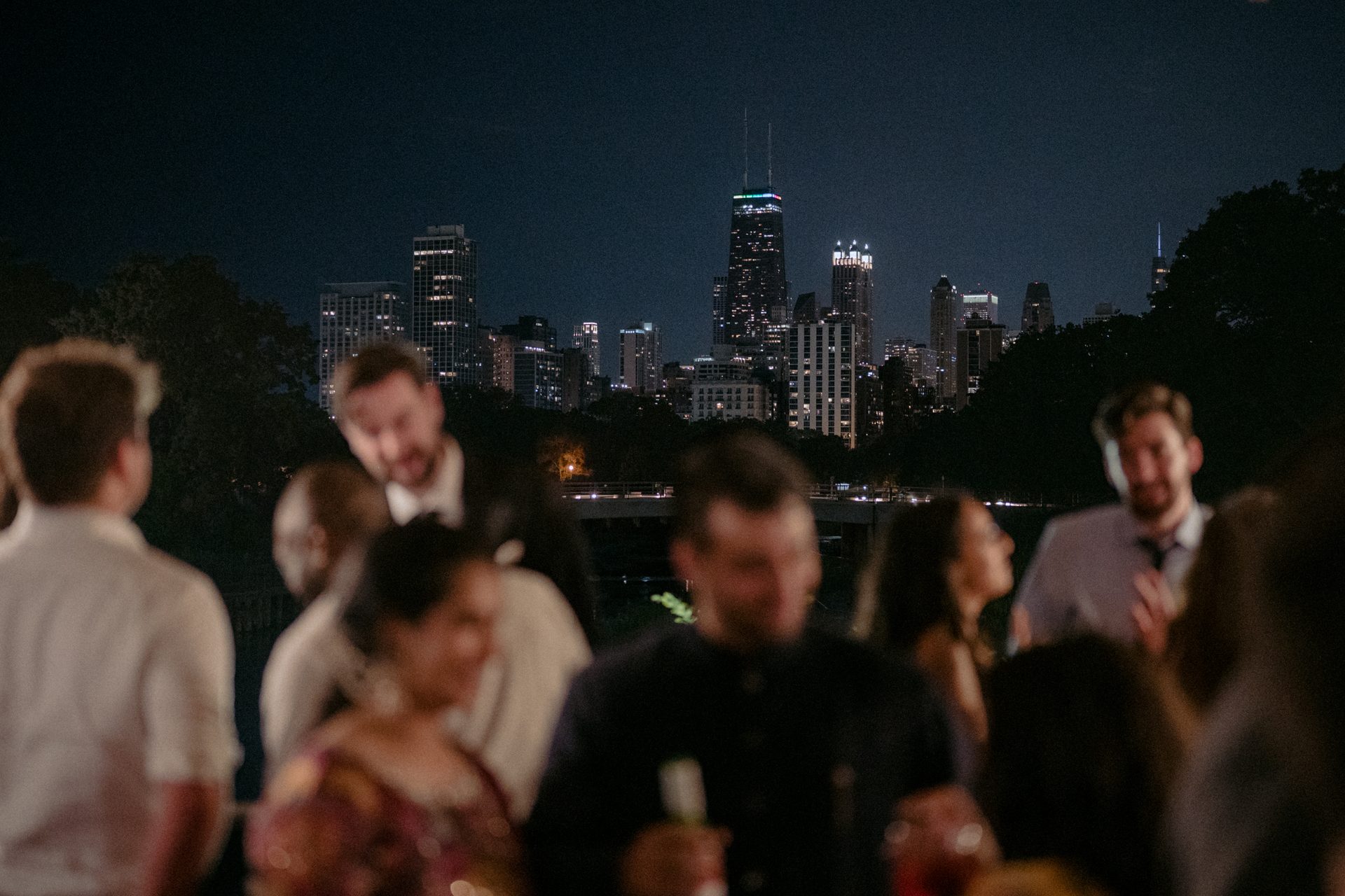 Blurred crowd at night with a brightly lit Chicago skyline in the background.