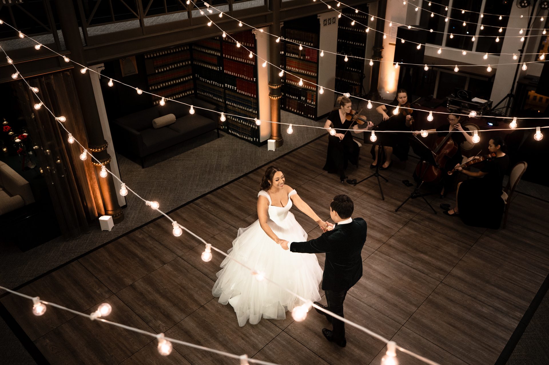Wedding couple dancing under string lights with a live string quartet.