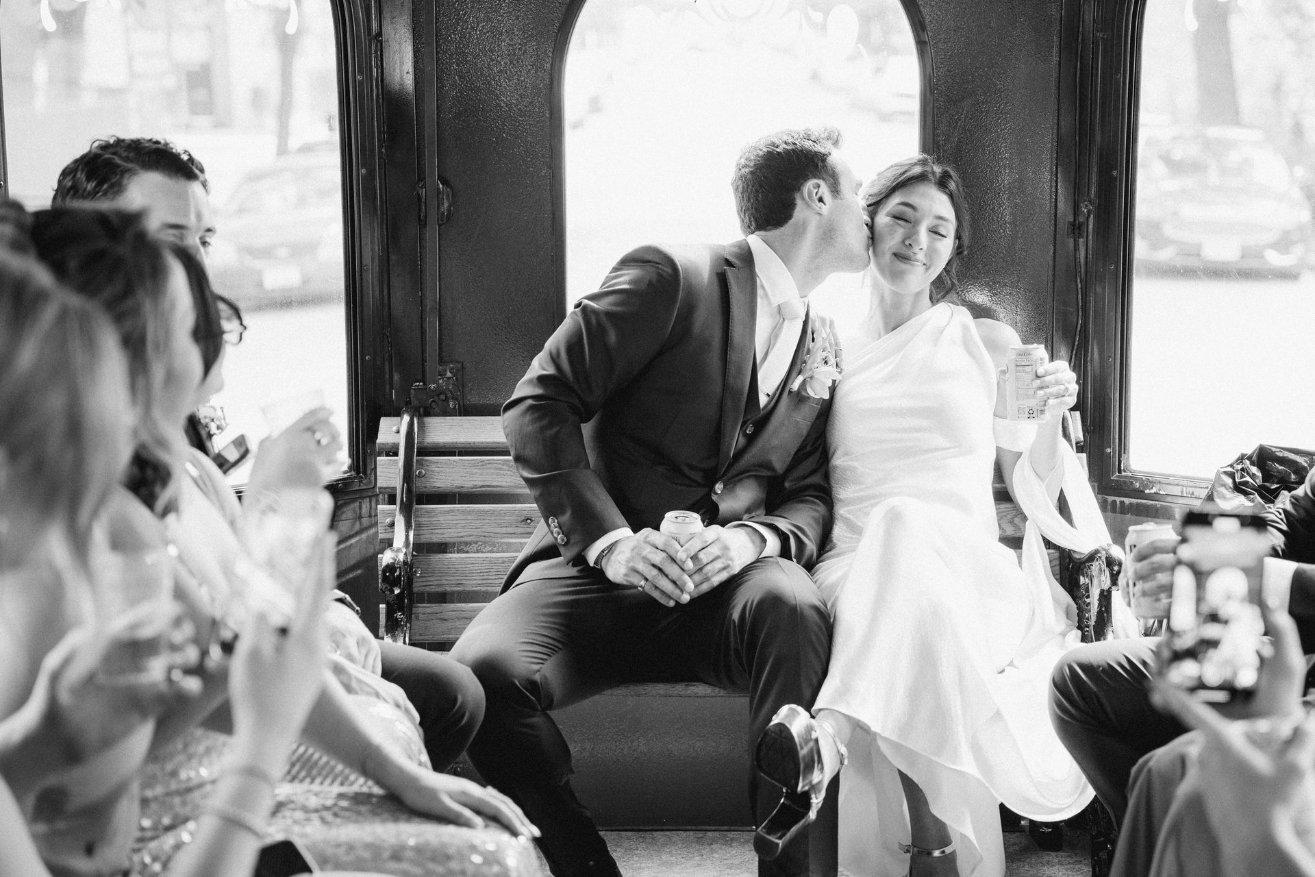 Black and white photo of a groom kissing his bride on the cheek inside a vehicle.