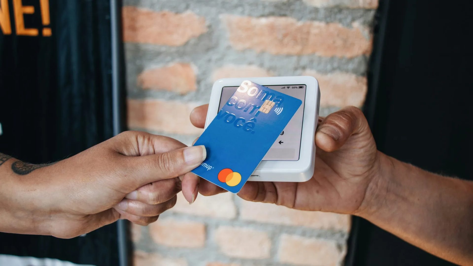 Hands holding a blue credit card to a white payment terminal.