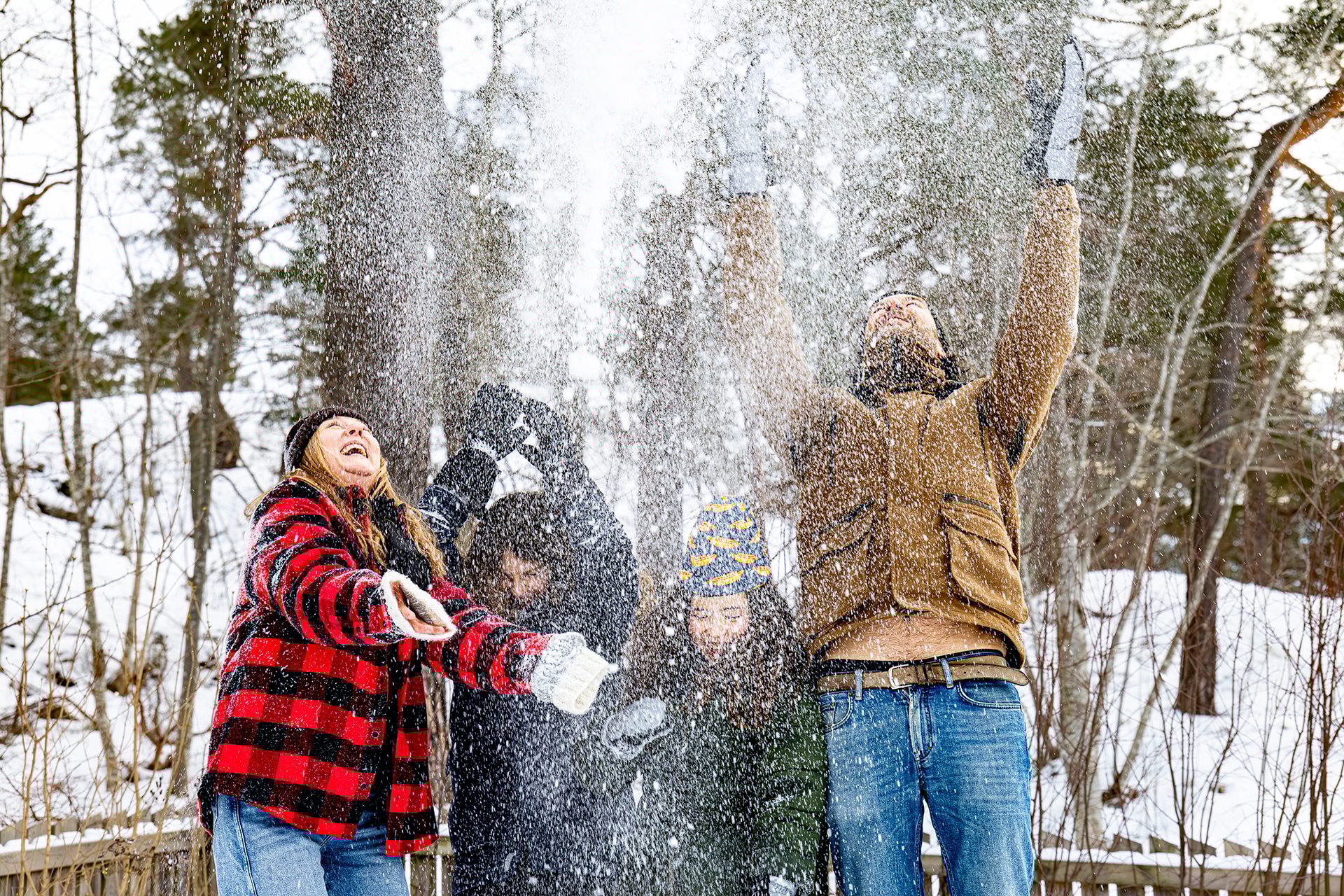 Happy people enjoying winter, throwing snow in the air with joyful expressions in a snowy forest.