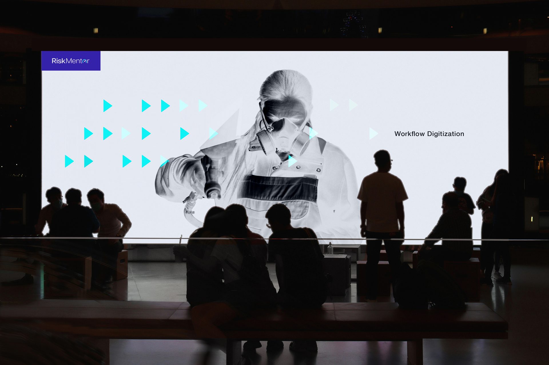 People watching a large screen with "RiskMentor" logo, "Workflow Digitization" text, and an inverted image of a person in a mask.