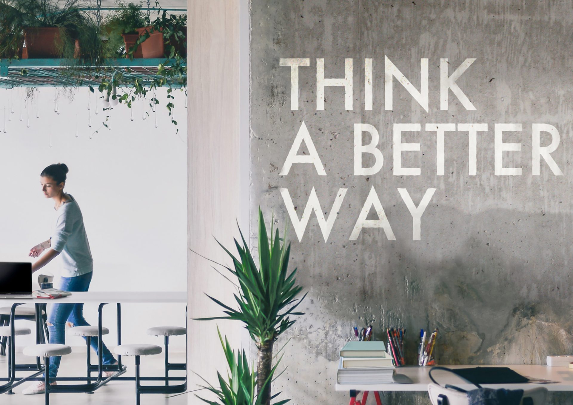 Woman in modern office with "THINK A BETTER WAY" on concrete wall and plants.