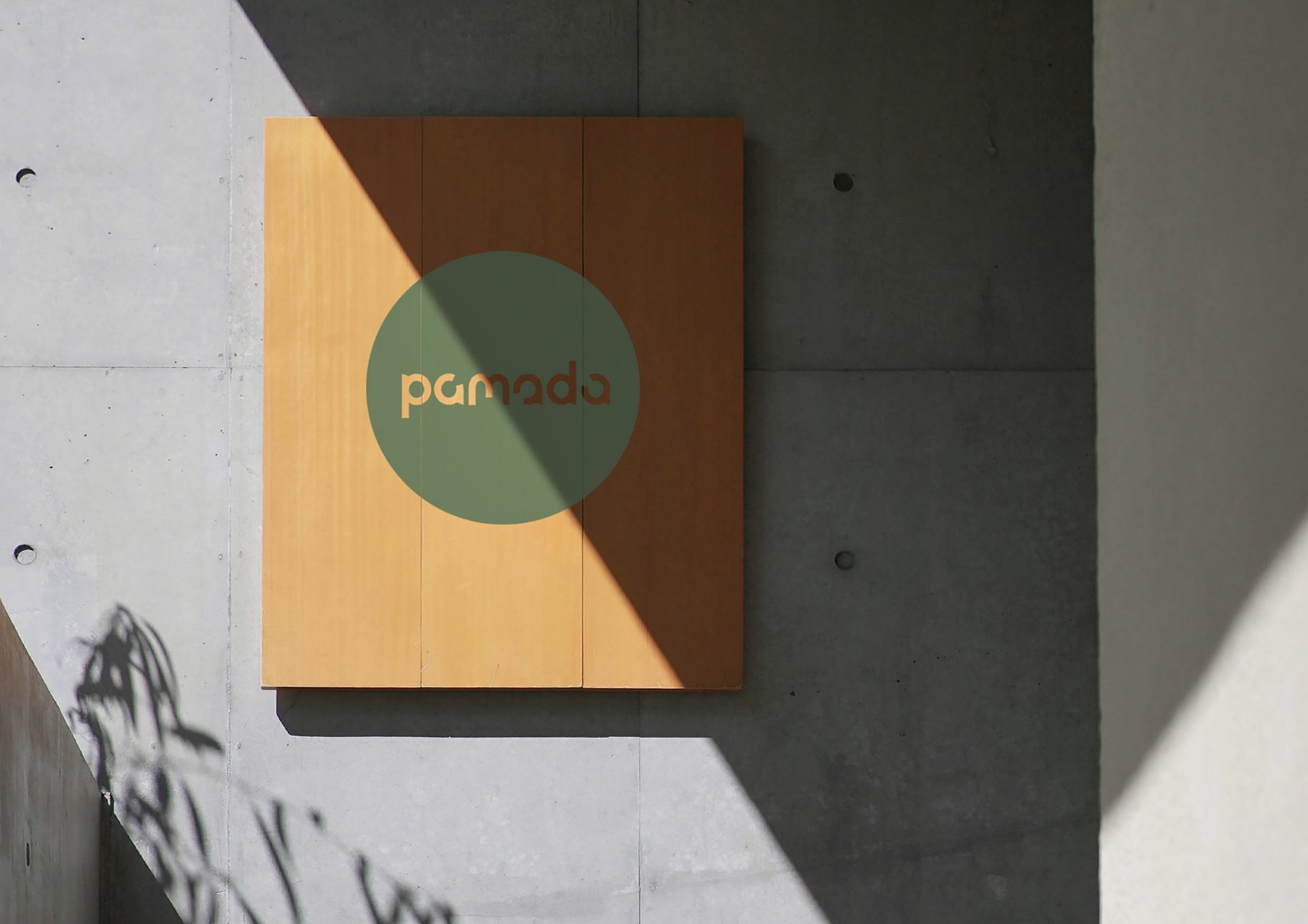 Wooden 'pamada' sign with green circle mounted on a concrete wall, showing strong shadows.