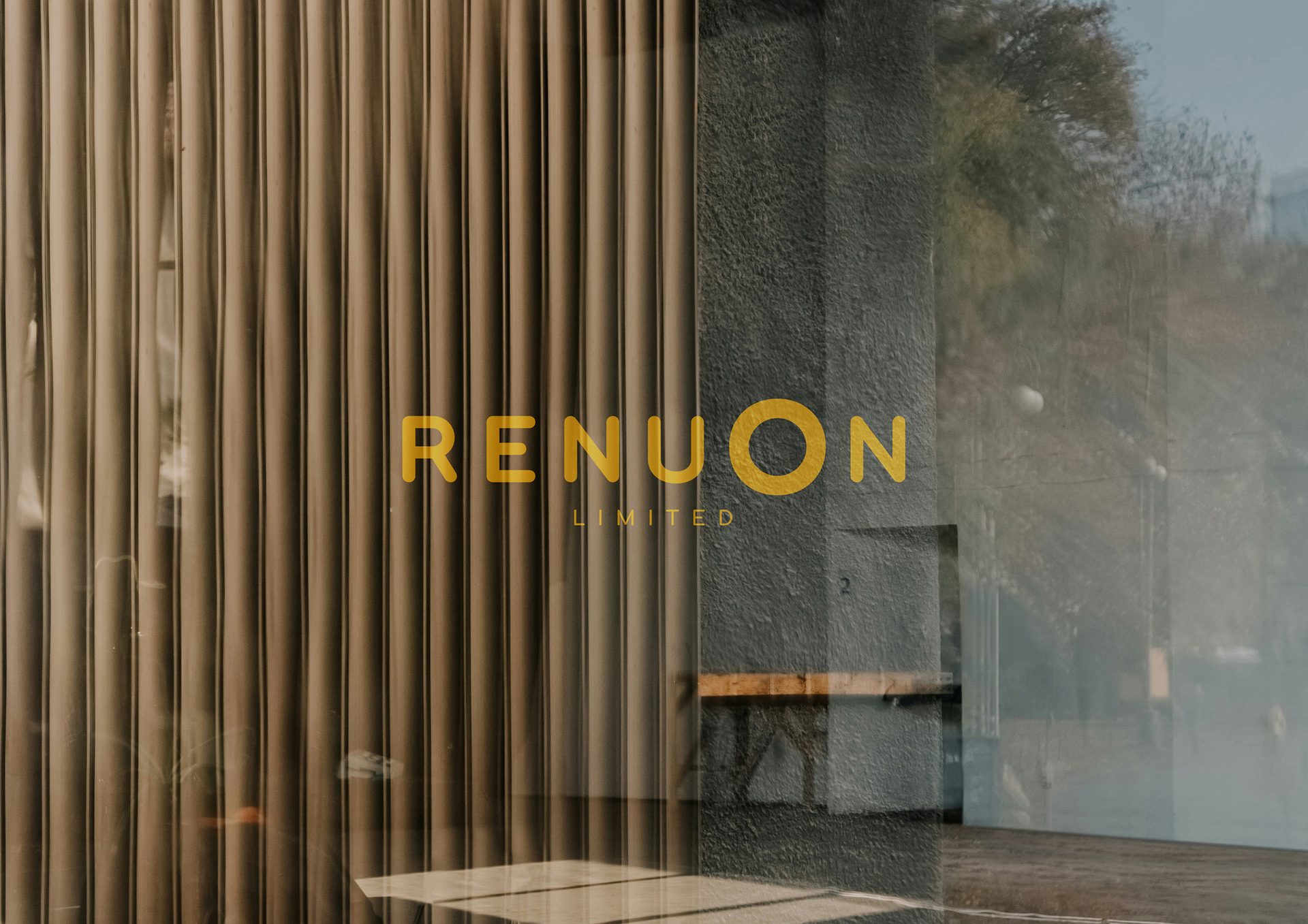 Yellow "RENUON LIMITED" on a glass window, with blinds, textured wall, and outdoor reflections.