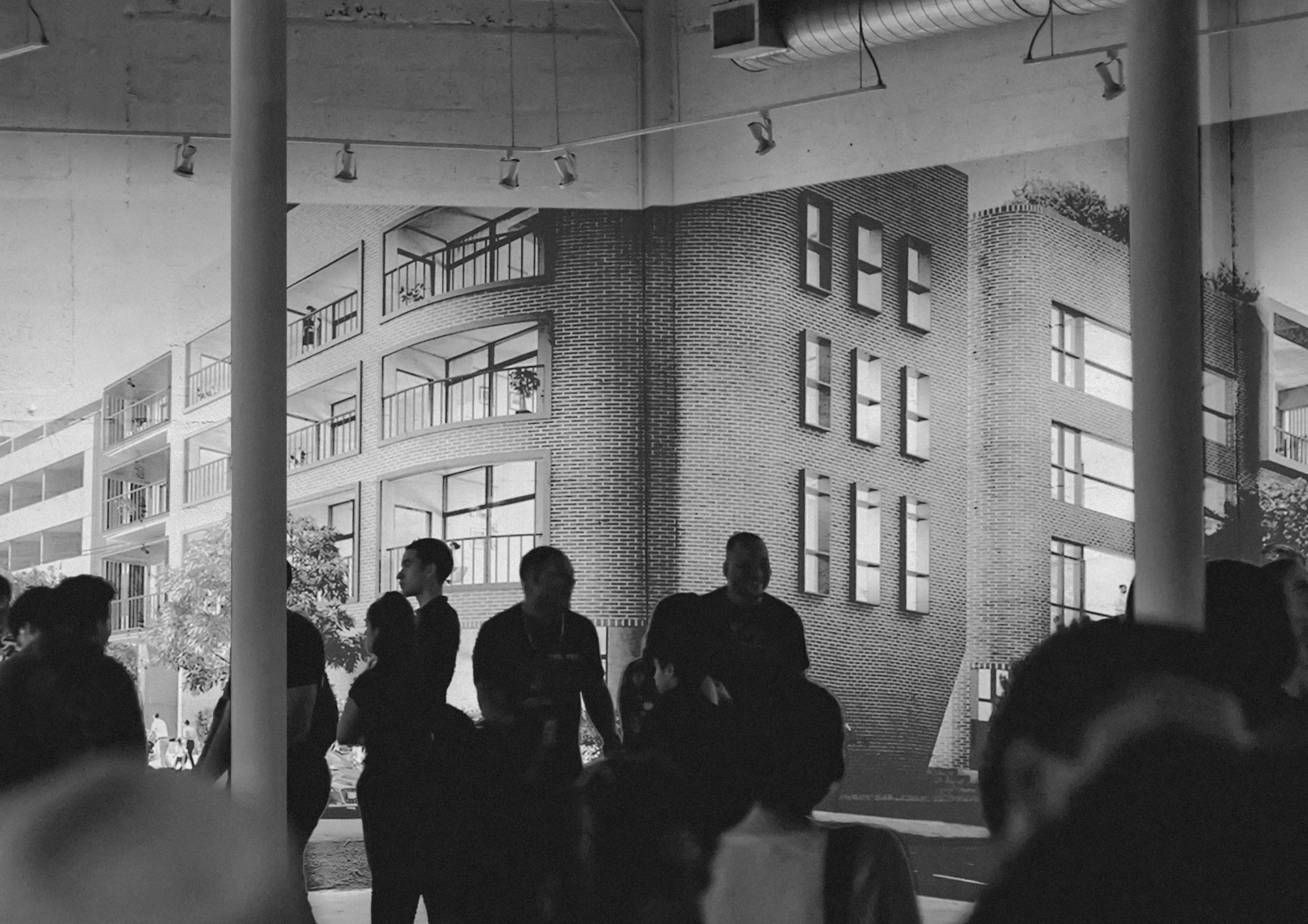 B&W image: Silhouetted figures indoors, with a large mural of a modern brick building in the background.