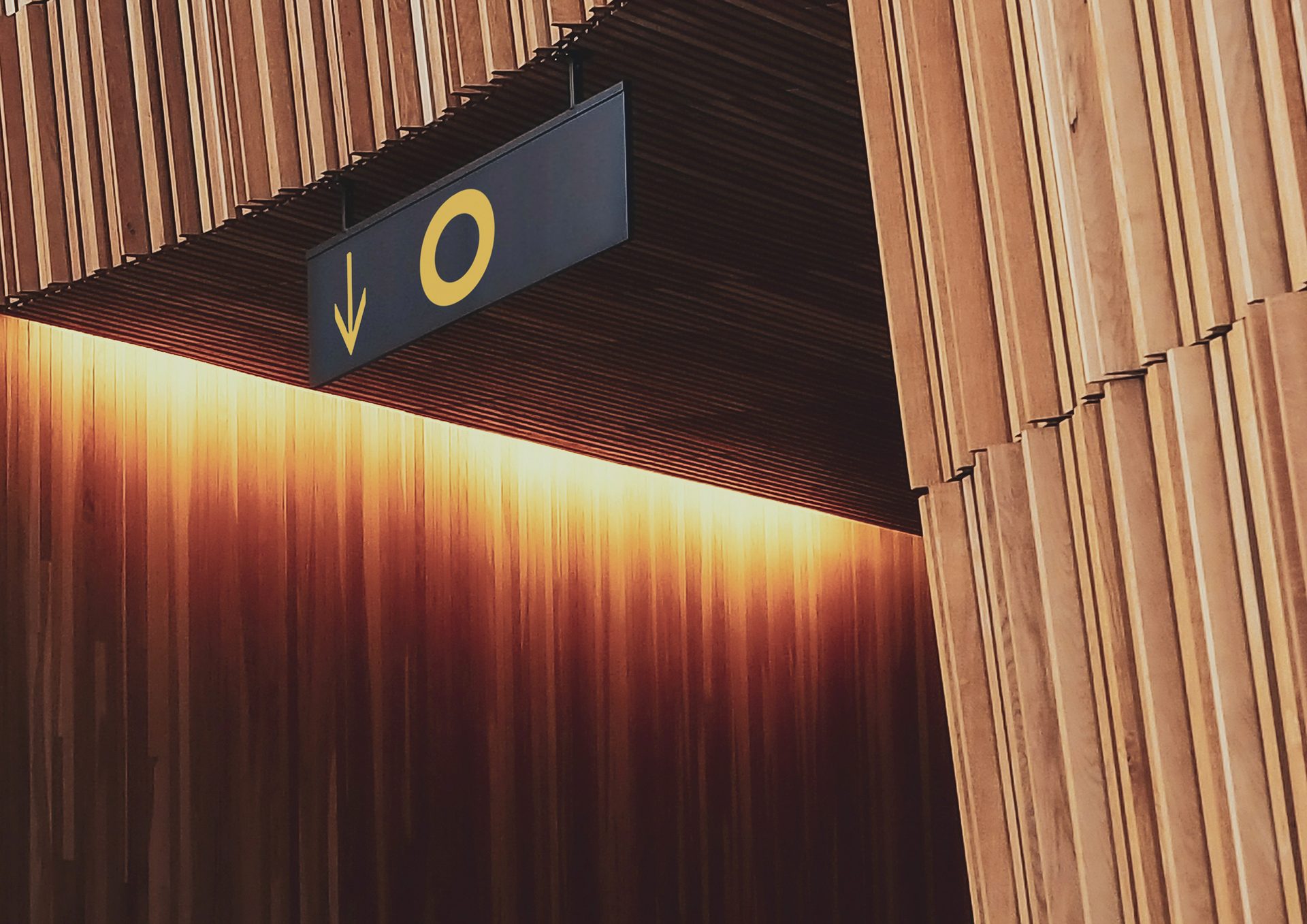 Wooden slatted interior, warmly lit, with a black sign displaying a yellow 'O' and down arrow.