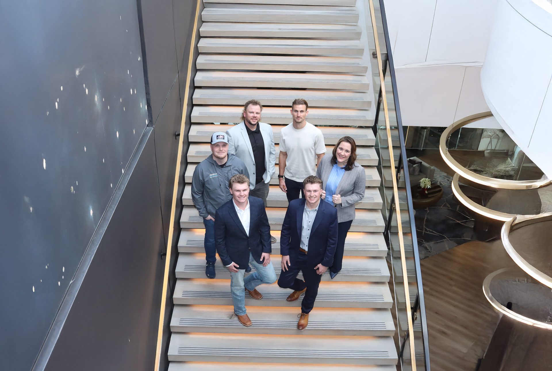 Six diverse people, including five men and one woman, pose together on a modern office staircase.