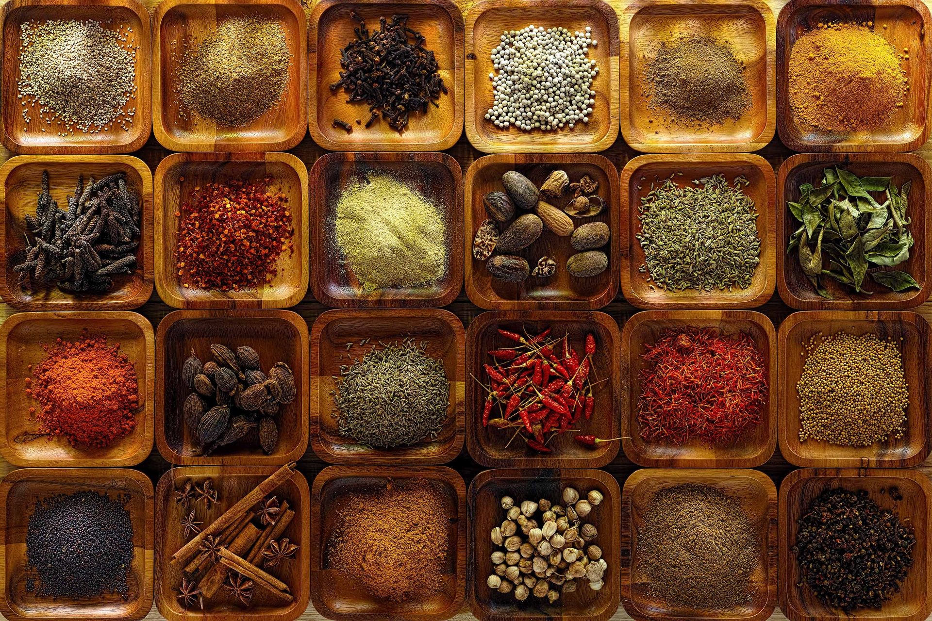 Variety of whole and ground spices displayed in small wooden bowls.