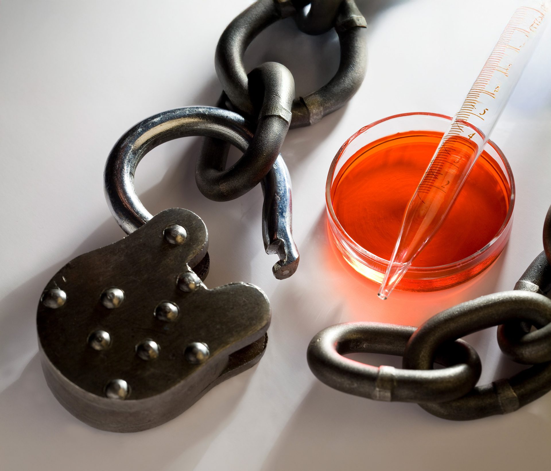 Broken chain, open padlock, petri dish with orange liquid, and a pipette.