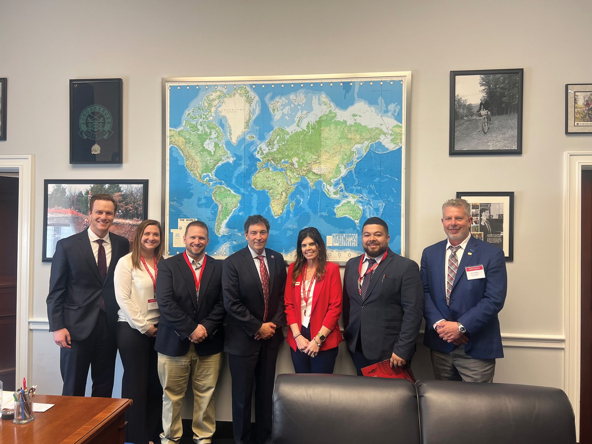 A group of 7 professionals, 4 men and 3 women, stand in an office with a world map behind them.