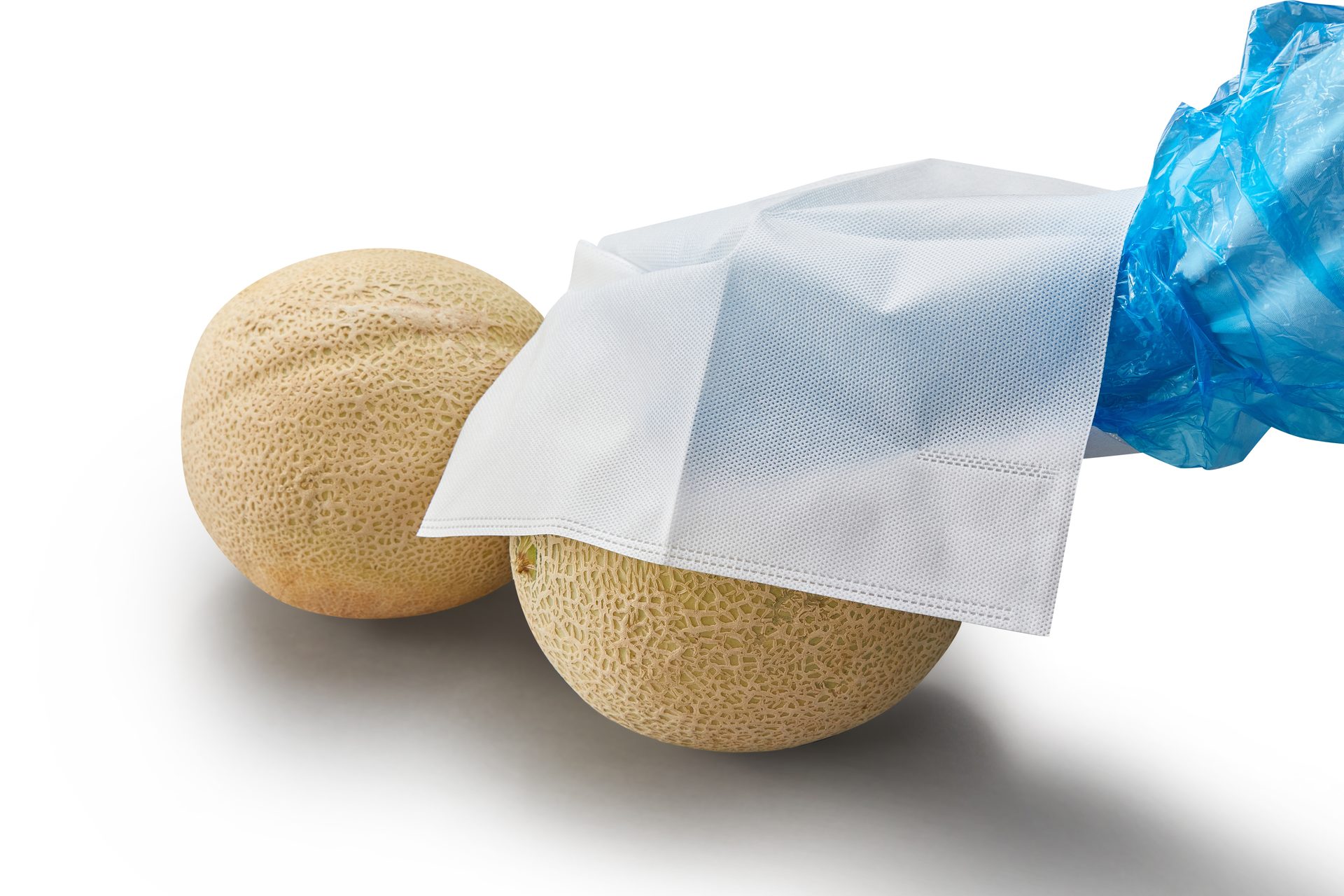 Two cantaloupes on a white background, one partially covered by white fabric and a blue plastic bag.