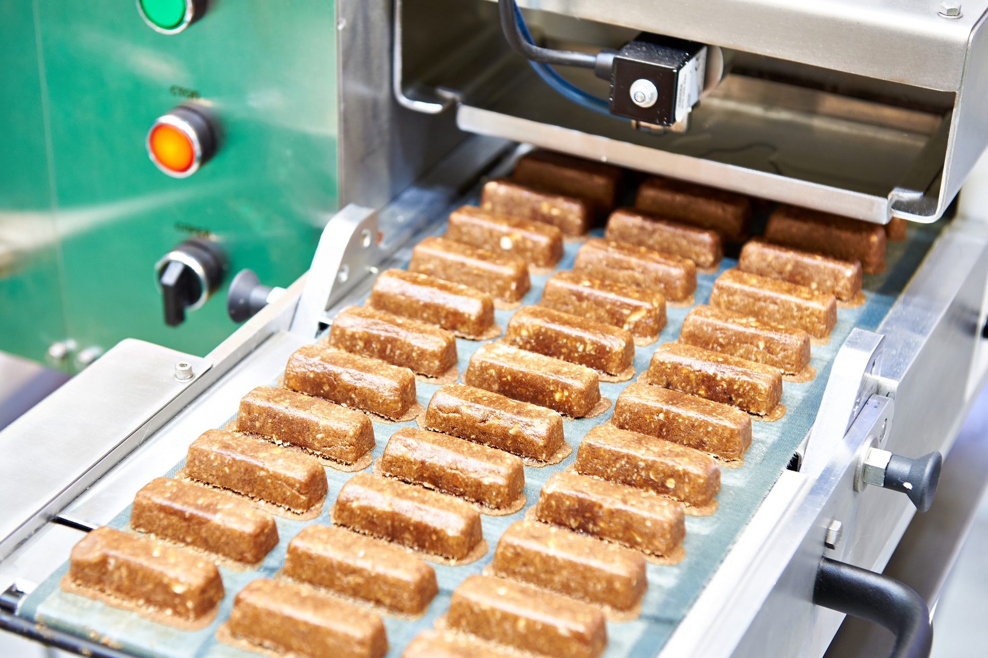 Conveyor belt in a food factory processing rows of brown snack bars, with machinery in the background.