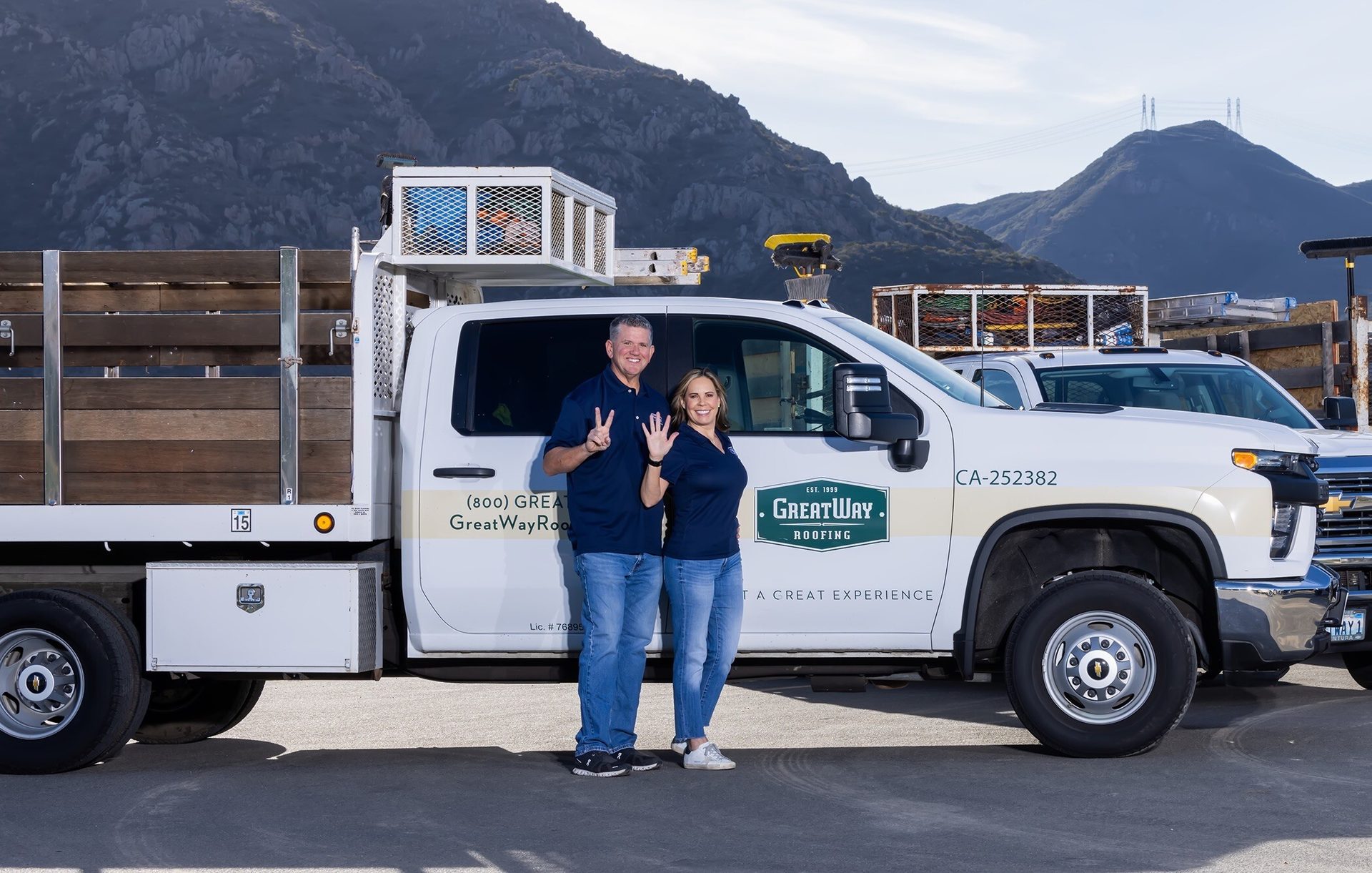 Man and woman pose by a GreatWay Roofing truck, mountains behind.