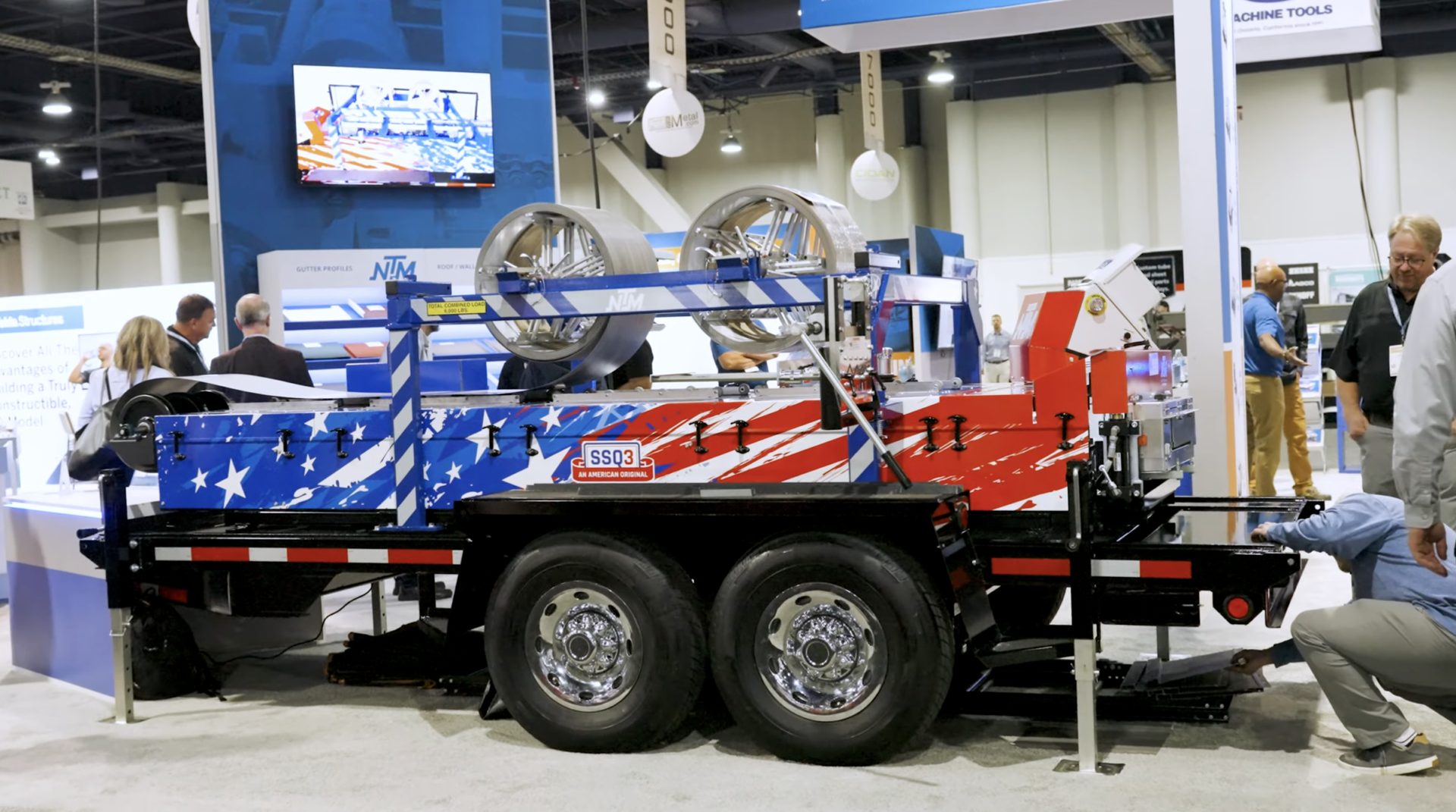 An American flag-painted SSQ3 trailer-mounted machine at a trade show, with people around it.